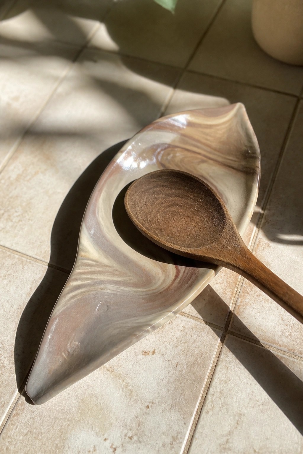 Wooden spoon in a marbled leaf-shaped ceramic dish on sunlit tiled floor