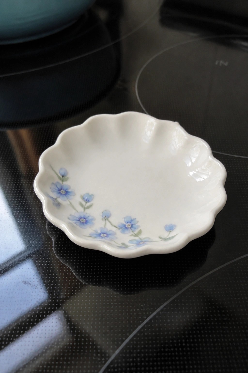 Small white scalloped bowl with blue flowers on black stovetop