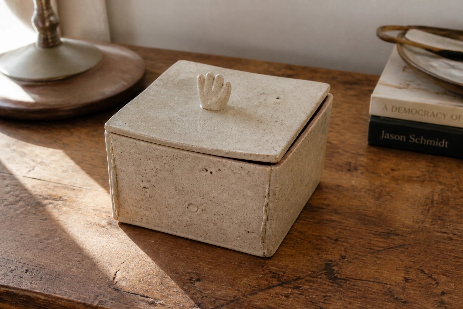 Beige ceramic box with tiny hand-shaped knob atop a wooden surface.