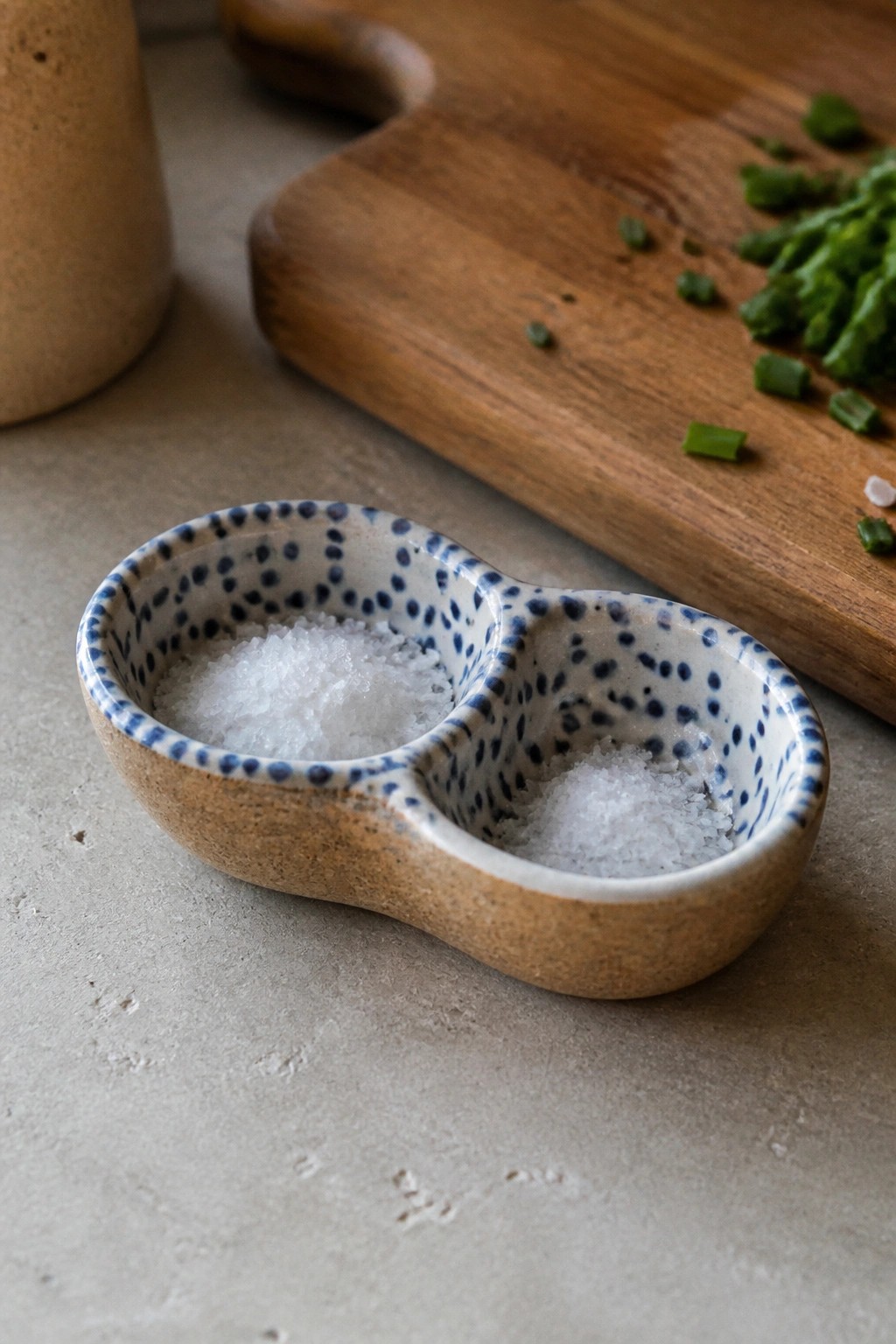 Speckled ceramic double salt dish filled with white crystals near chopped green onions