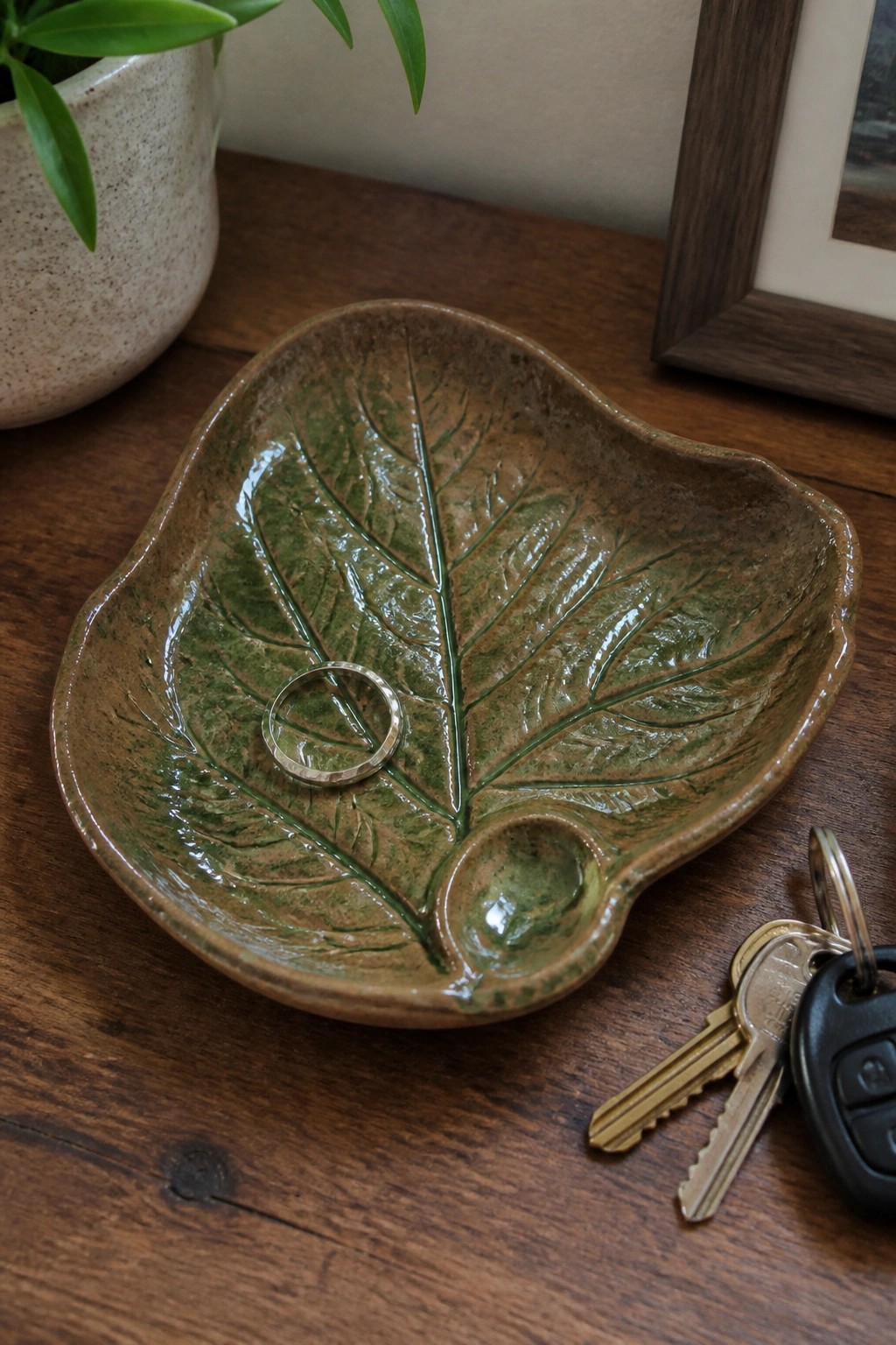 Leaf-shaped green ceramic bowl with silver ring and keys on wood