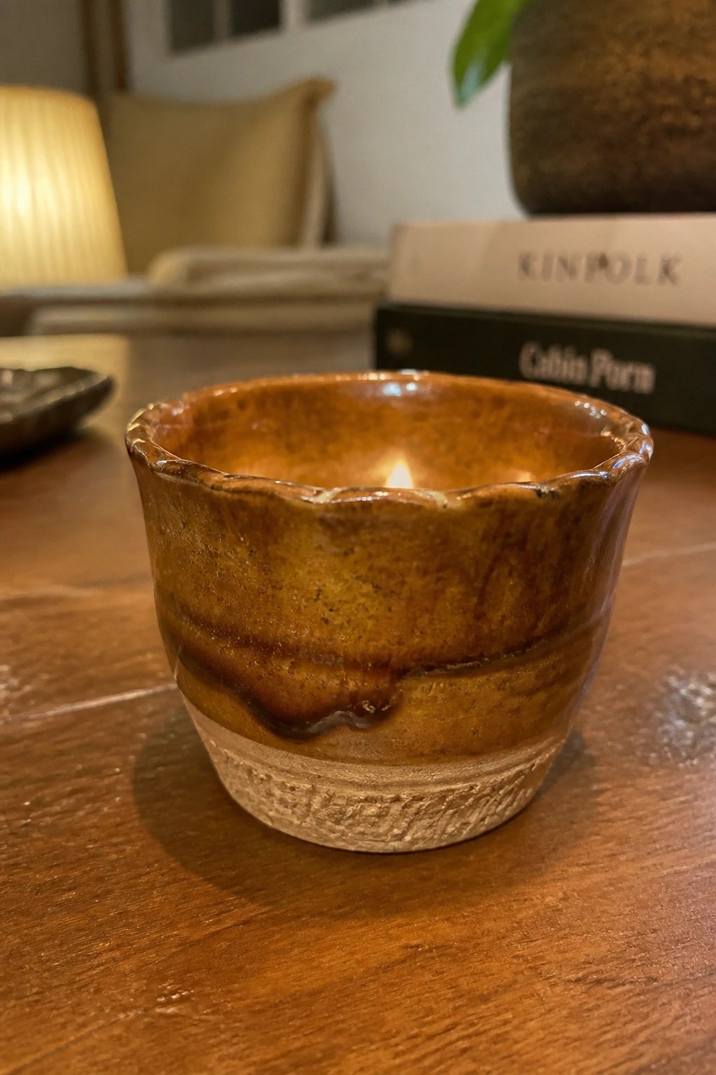 Brown glazed ceramic bowl with lit candle on wooden table