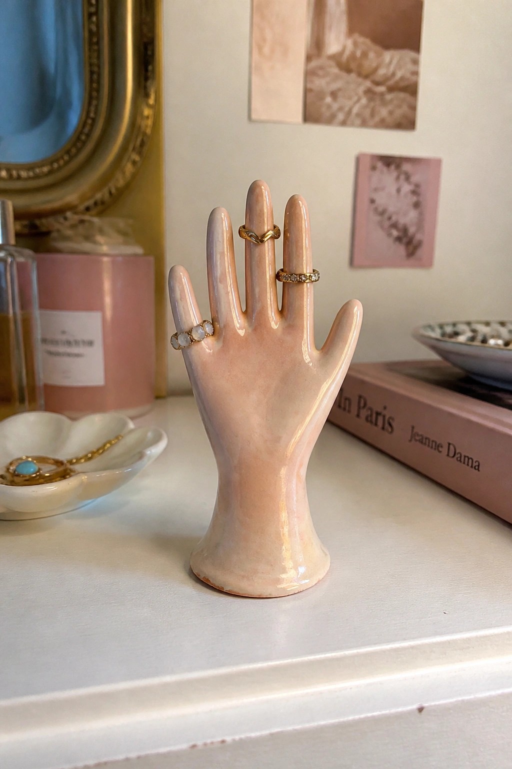 Pink ceramic hand ring holder with gold rings on white vanity table