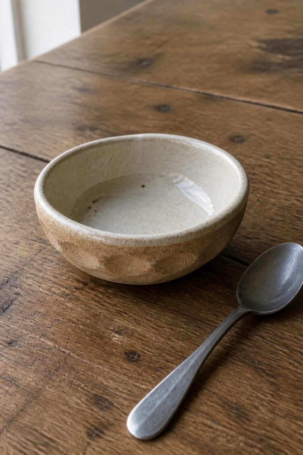 Speckled ceramic bowl with white liquid beside metal spoon on wooden table