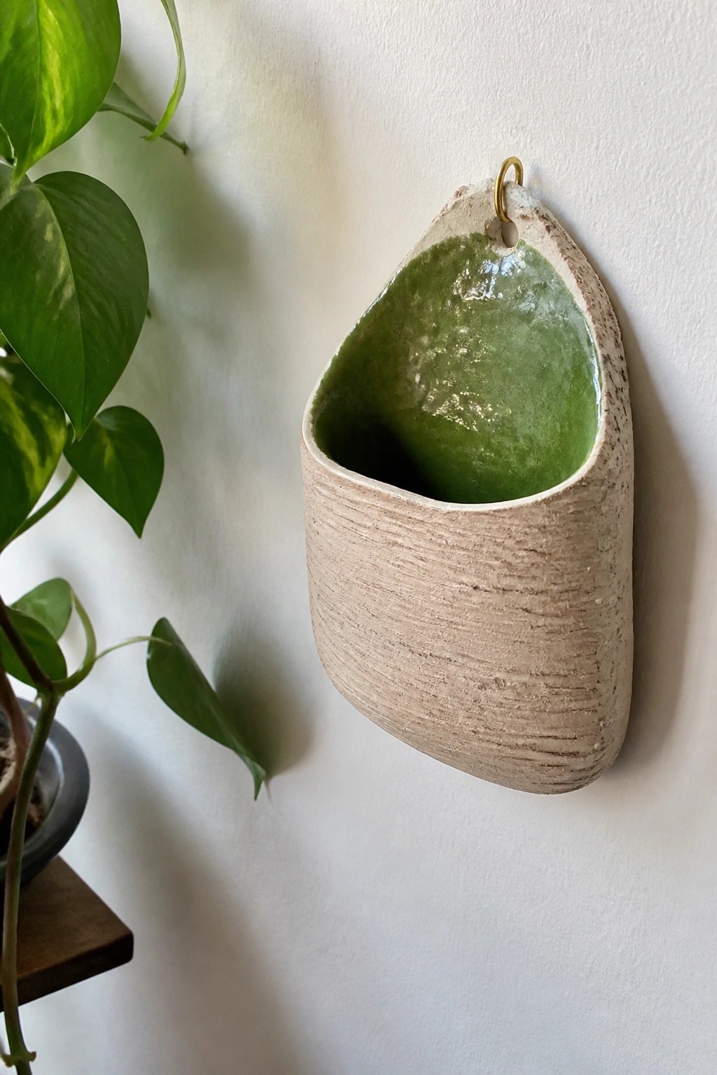 Textured beige ceramic wall pocket with glossy green interior on white wall.