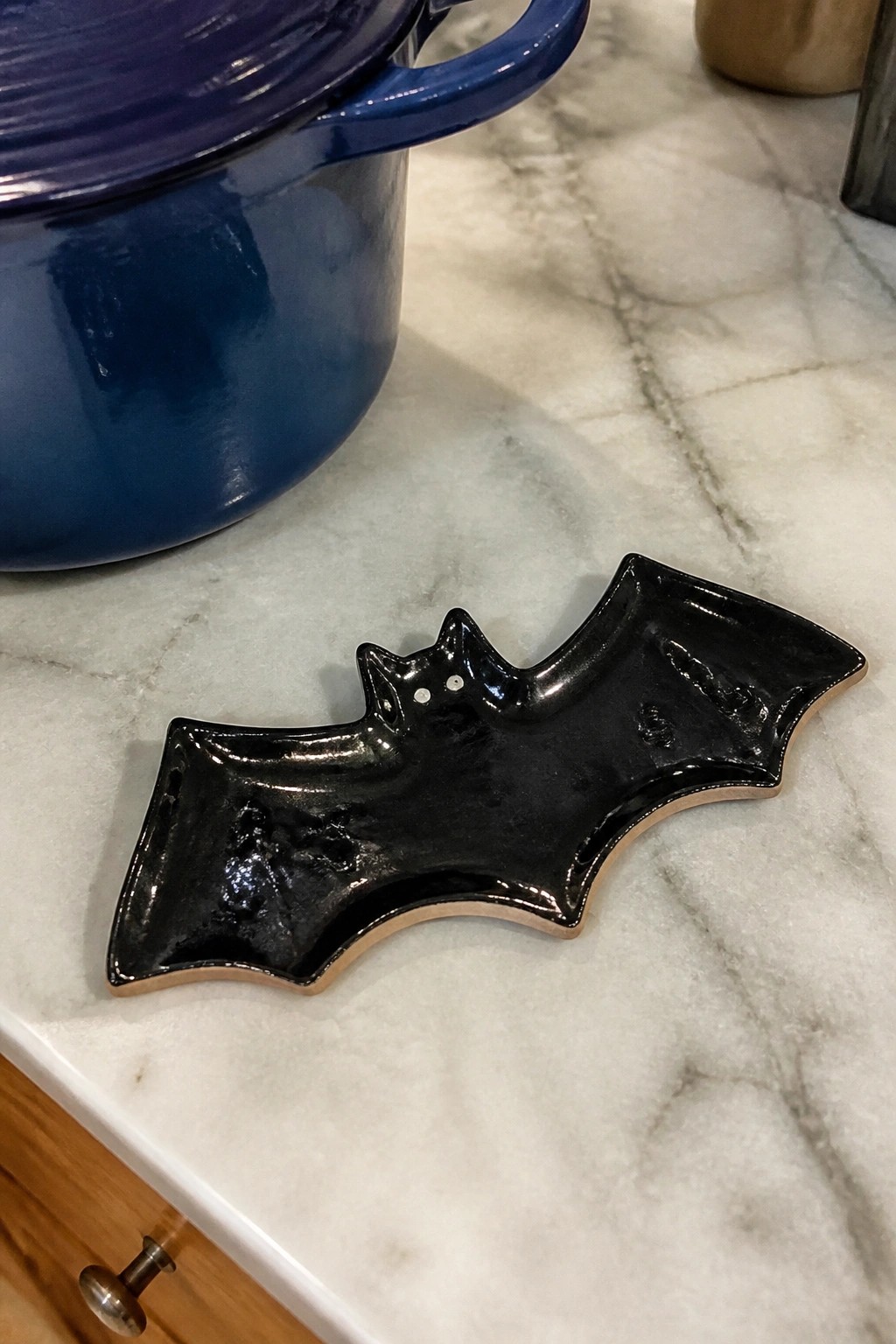 A glossy black ceramic dish shaped like a bat rests on a white marble countertop.