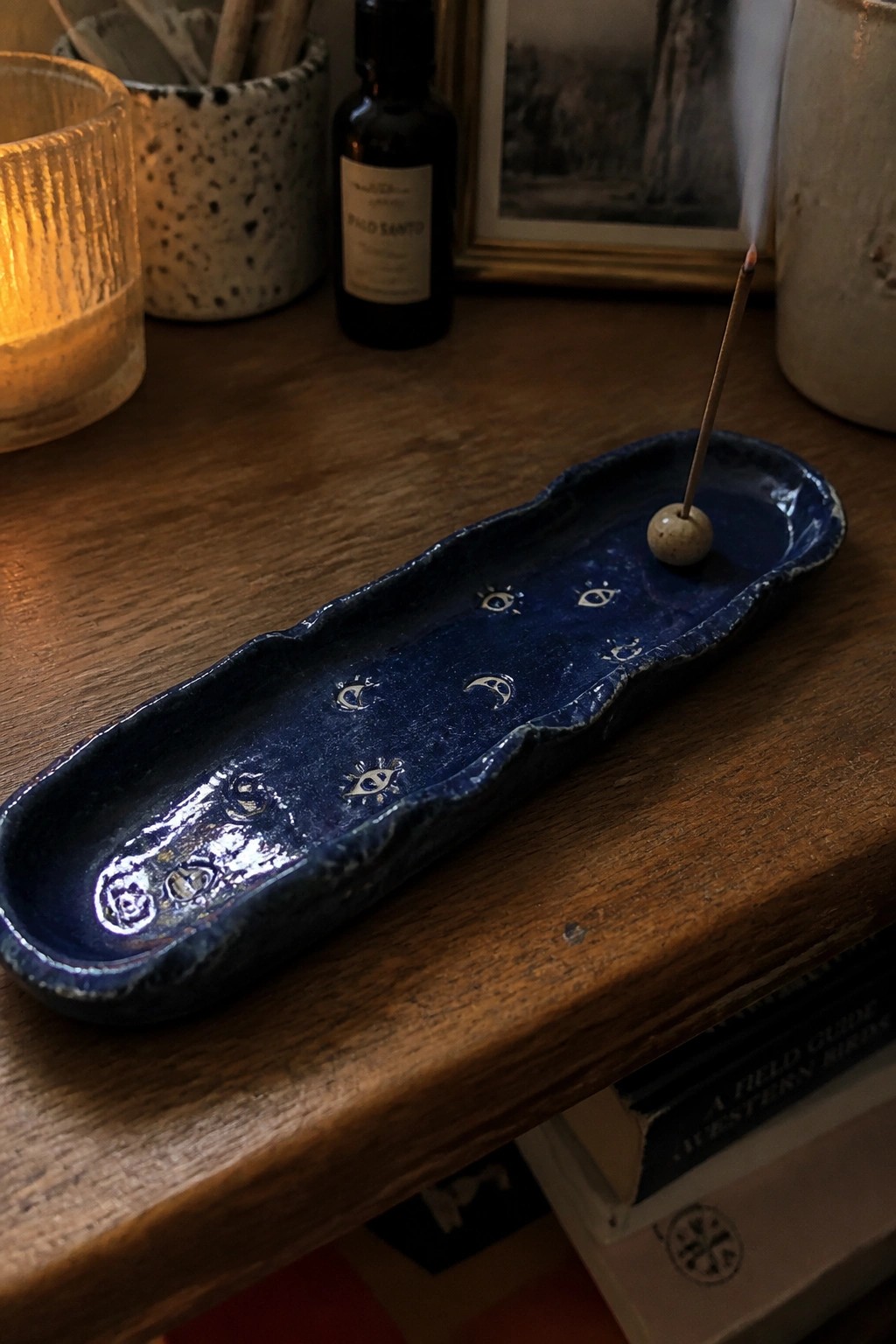 Blue ceramic incense holder with moon and eye symbols, lit stick on wooden table