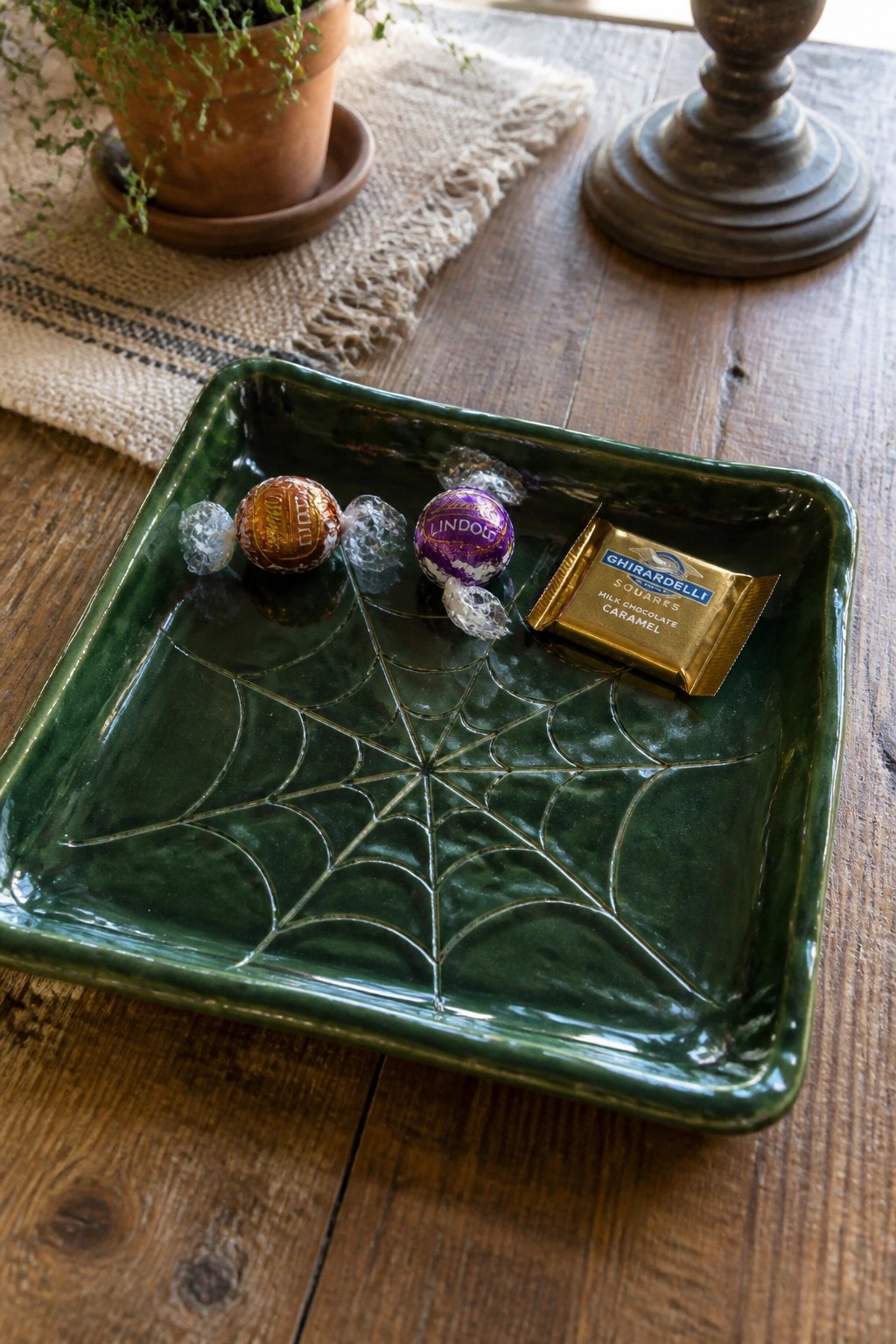 Green spiderweb dish with Lindor and Ghirardelli chocolates on wooden table beside plant