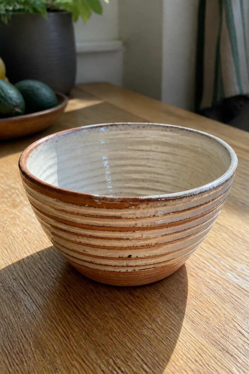 Striped ceramic bowl on wooden table with avocados and plant in background