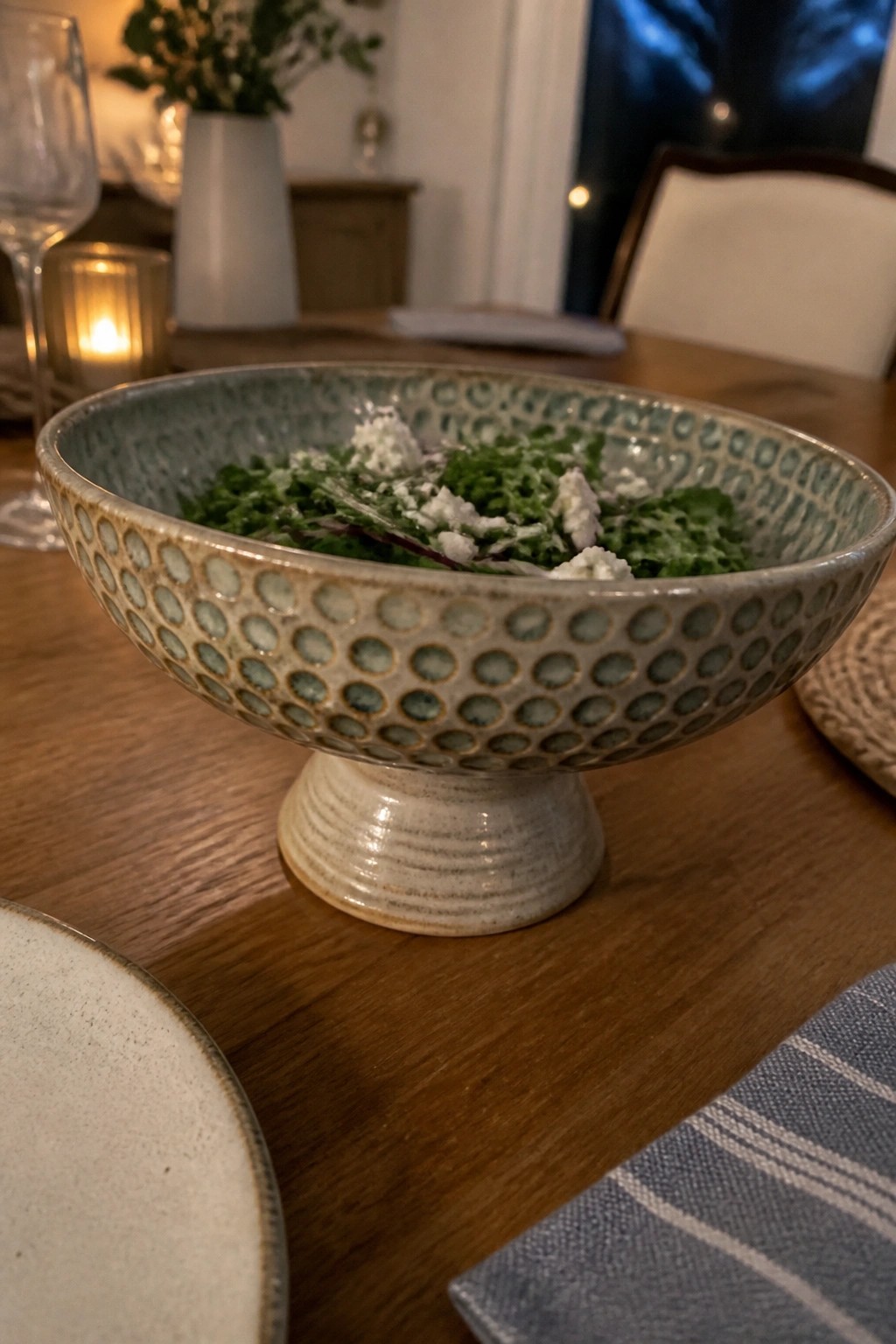 Ceramic pedestal bowl with dotted pattern holding green salad on wooden table.