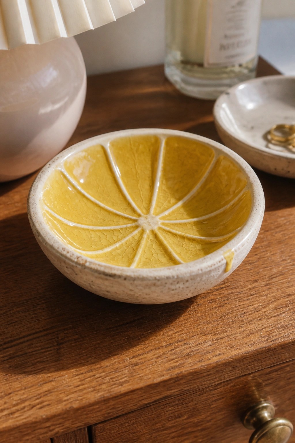 Yellow ceramic citrus-slice bowl on wooden table with pink lamp and candle.