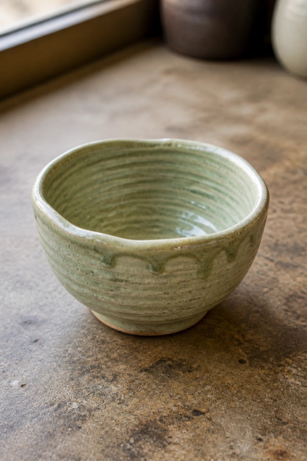 Light green ceramic bowl with ridged texture and dripping glaze on brown surface