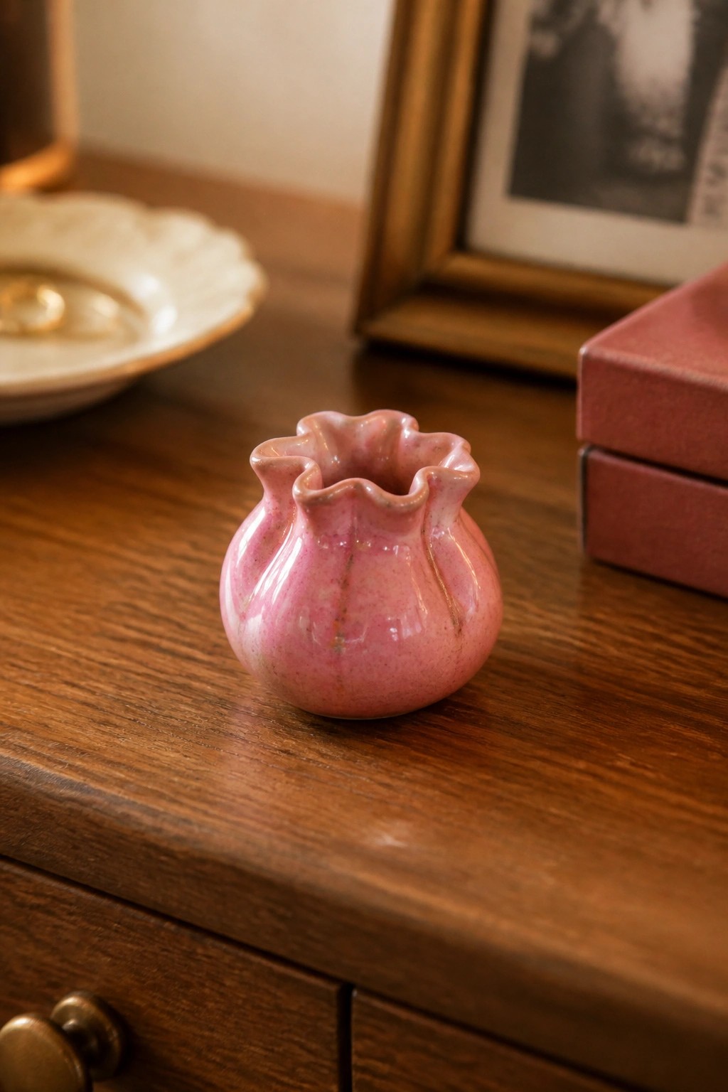 Small pink ceramic vase with ruffled rim on wooden dresser surface