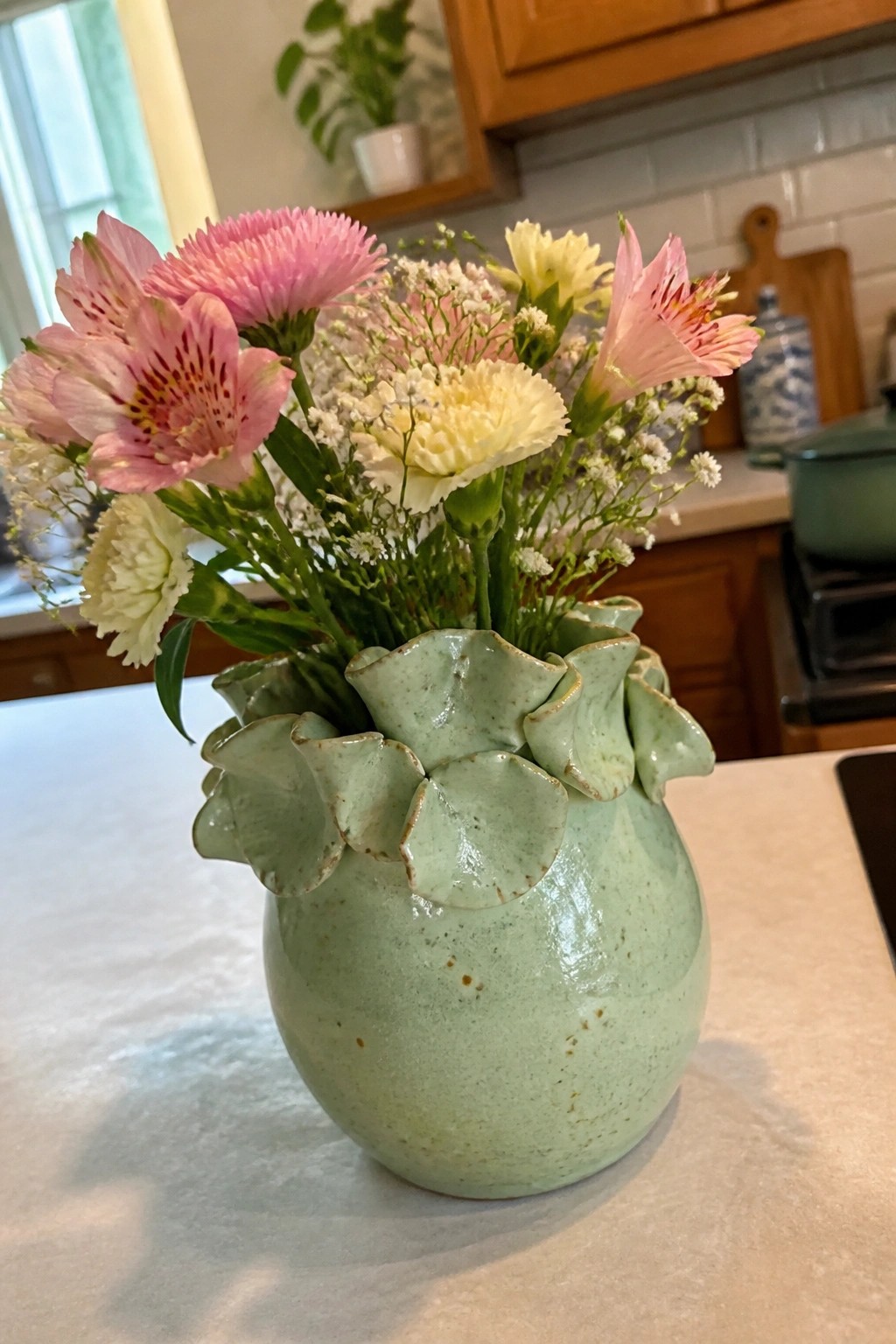 Light green ruffled ceramic vase with pink, yellow flowers on kitchen counter