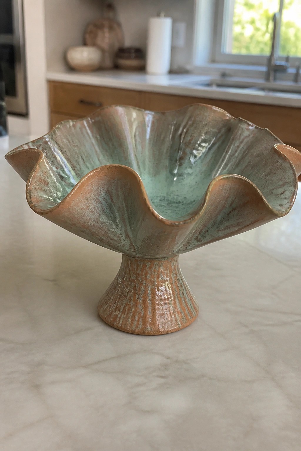 Ruffled ceramic pedestal bowl with turquoise and copper glaze on marble counter