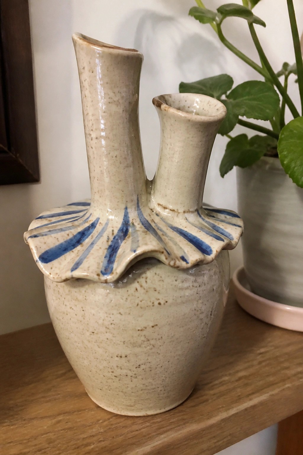 Ceramic vase with two spouts and blue-striped ruffled collar on wooden shelf