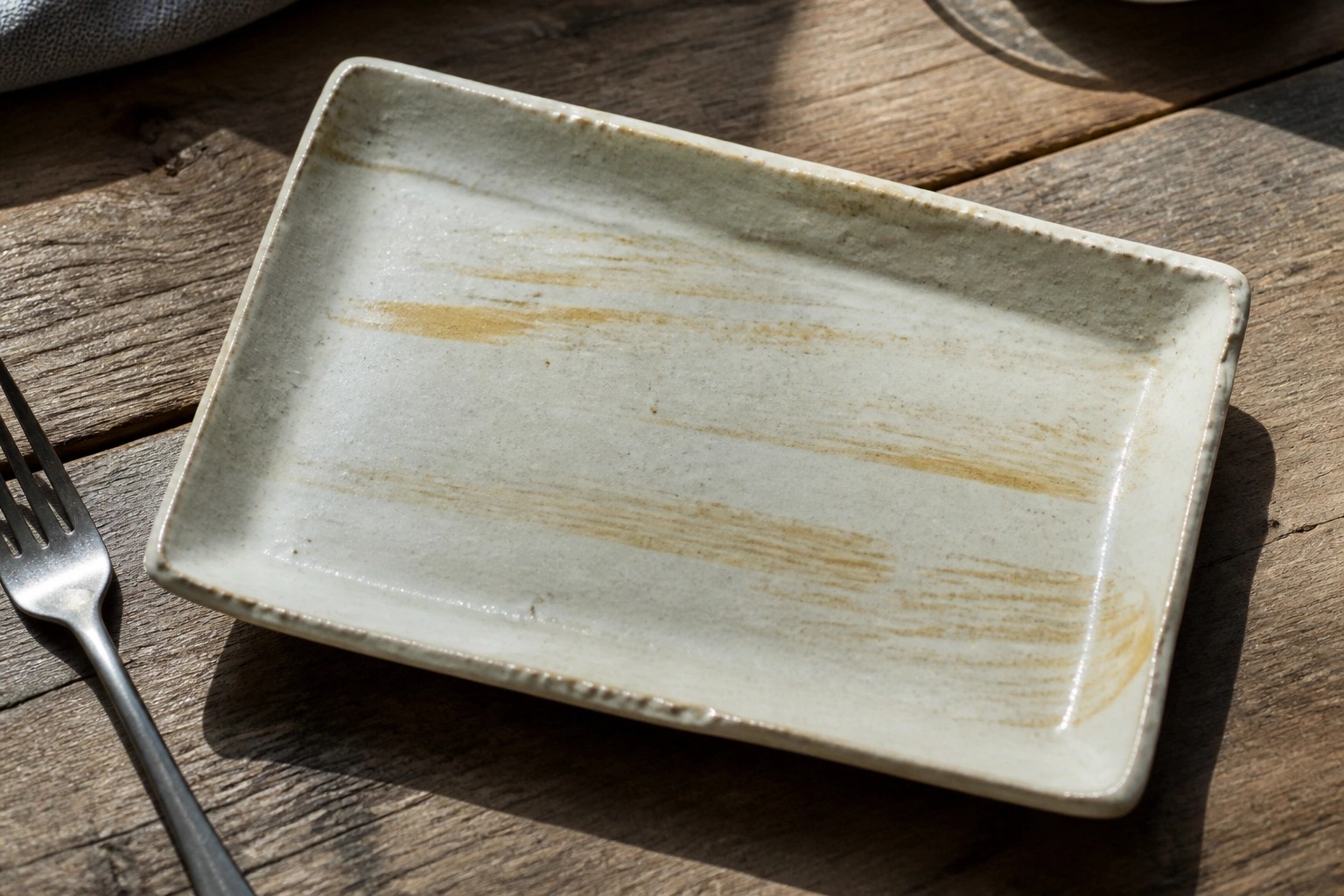 Rectangular white ceramic plate with brown streaks on wooden table beside fork