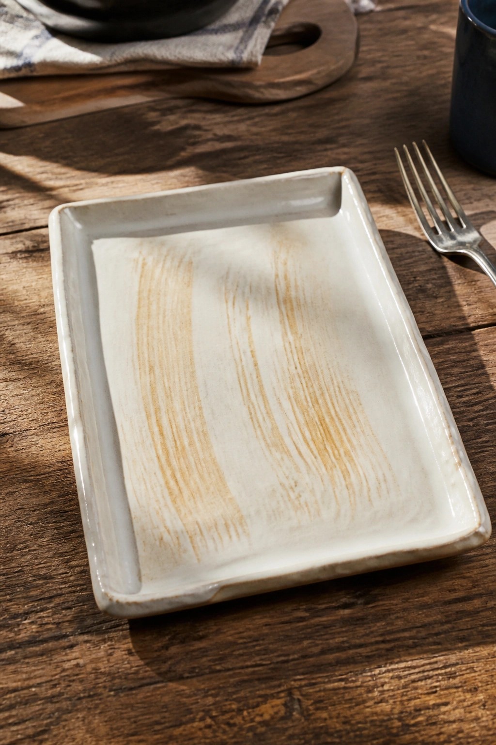 Rectangular white ceramic plate with brown streaks on wooden table beside fork