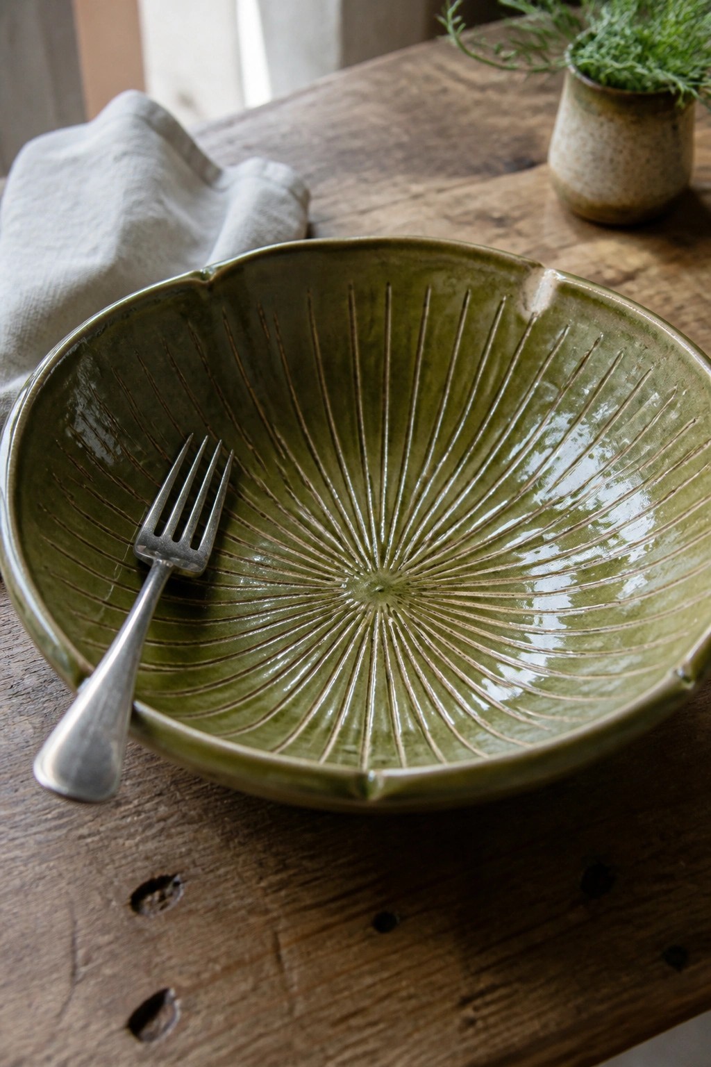 Green ceramic bowl with radiating lines holds a silver fork on wooden table.