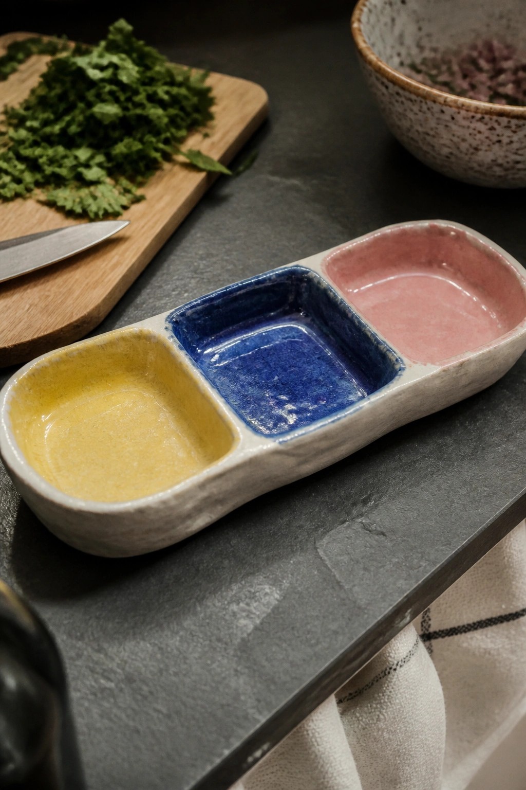 Tri-compartment ceramic dish with yellow, blue, and pink glazes on dark counter