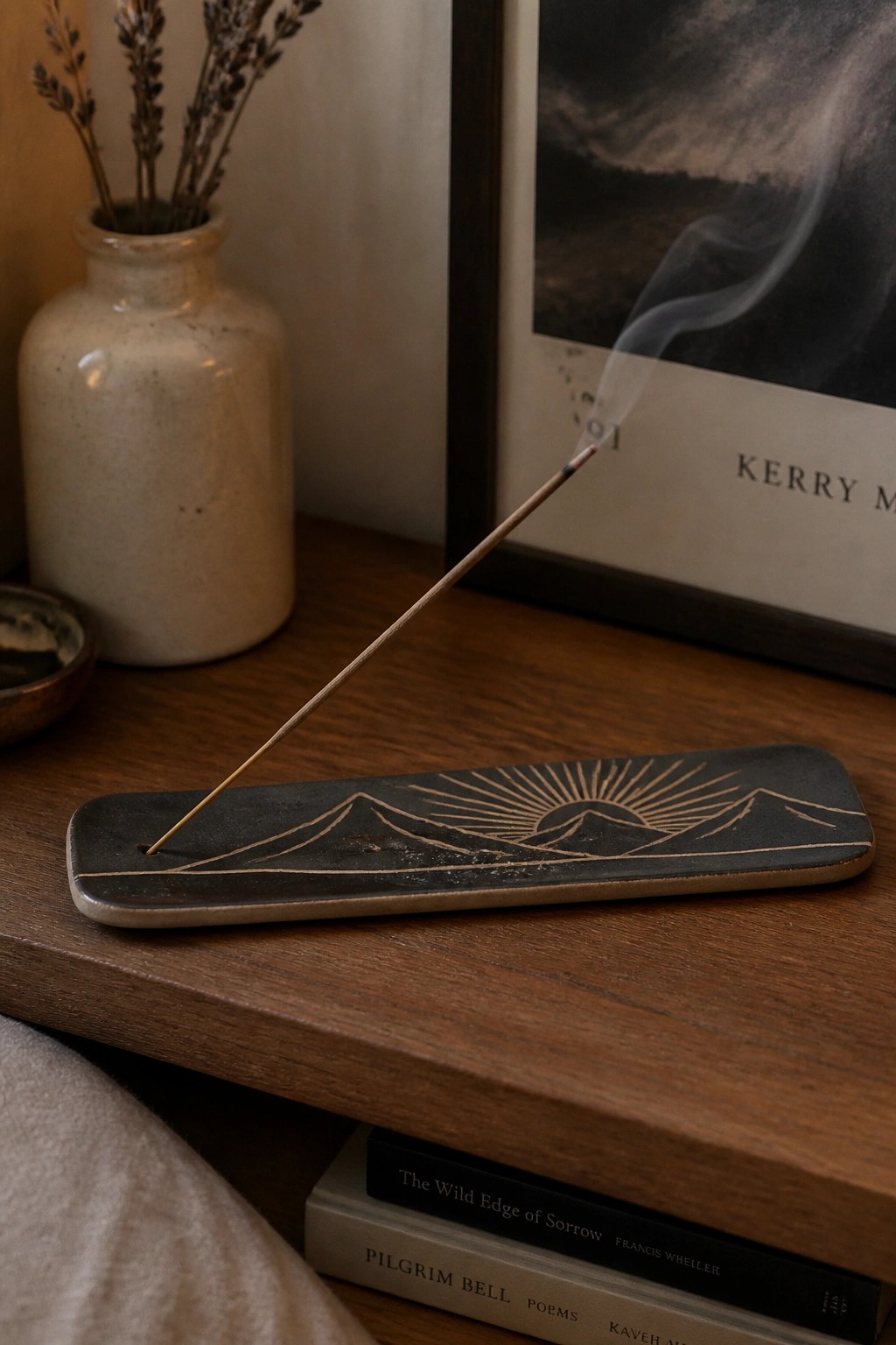 Burning incense on black ceramic holder with mountain and sun engraving on wood