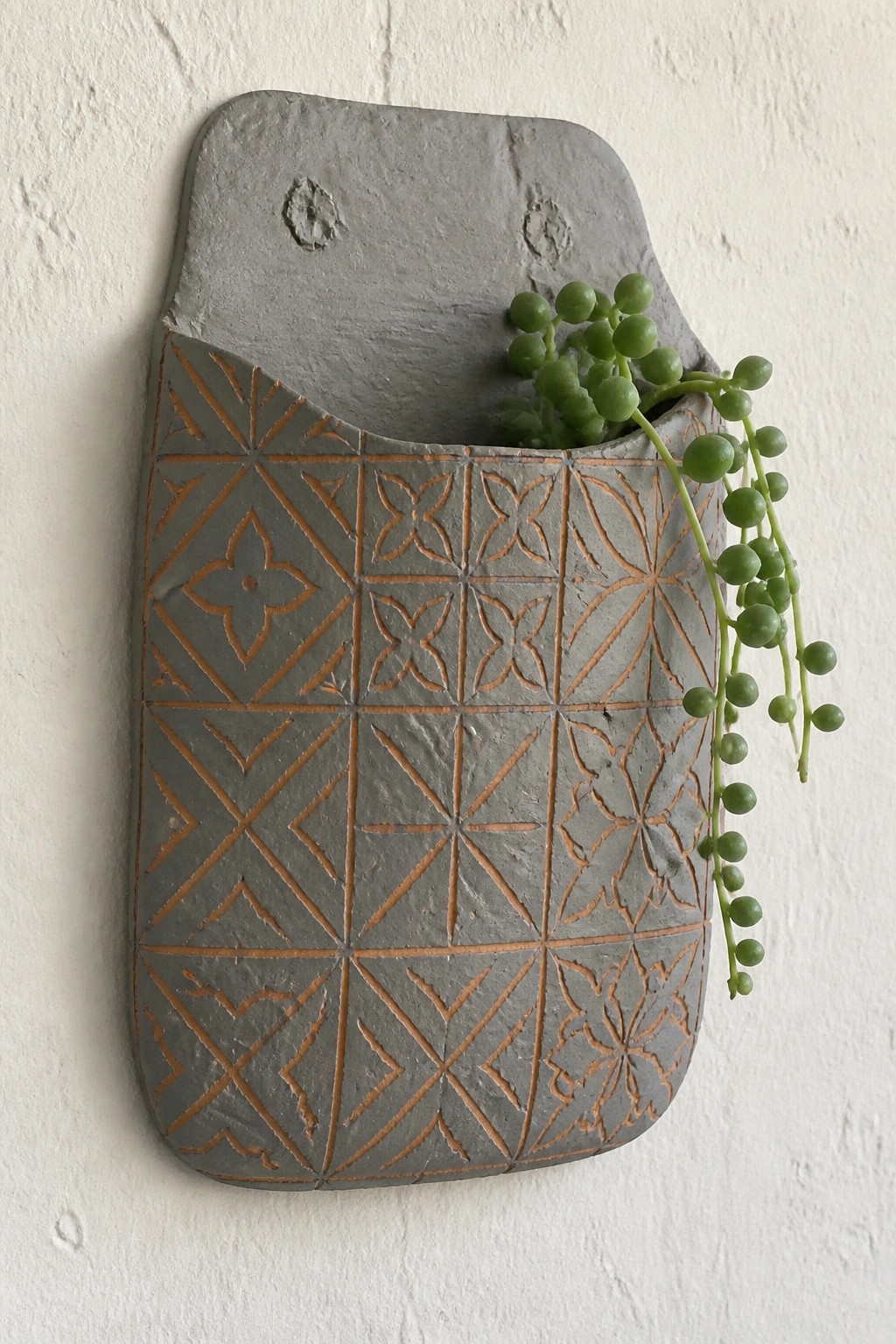 Gray wall-mounted planter with orange geometric patterns holding a trailing green plant.