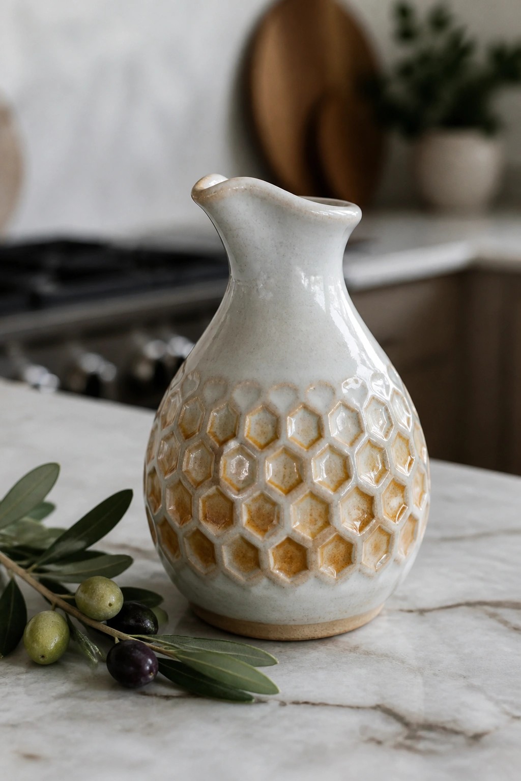 White ceramic pitcher with honeycomb pattern beside olive branch on marble counter