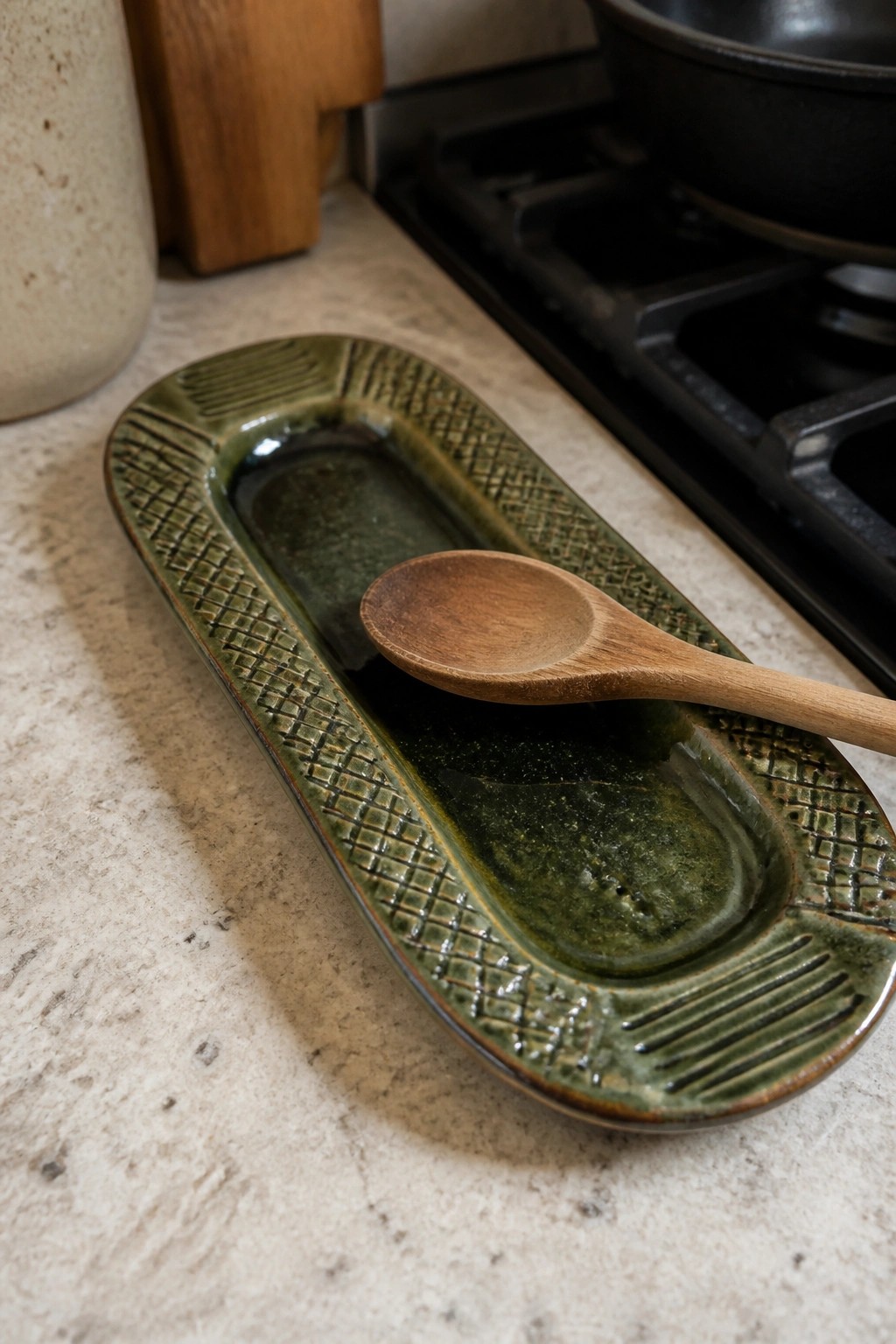 Green textured ceramic dish with wooden spoon in dark liquid on kitchen counter
