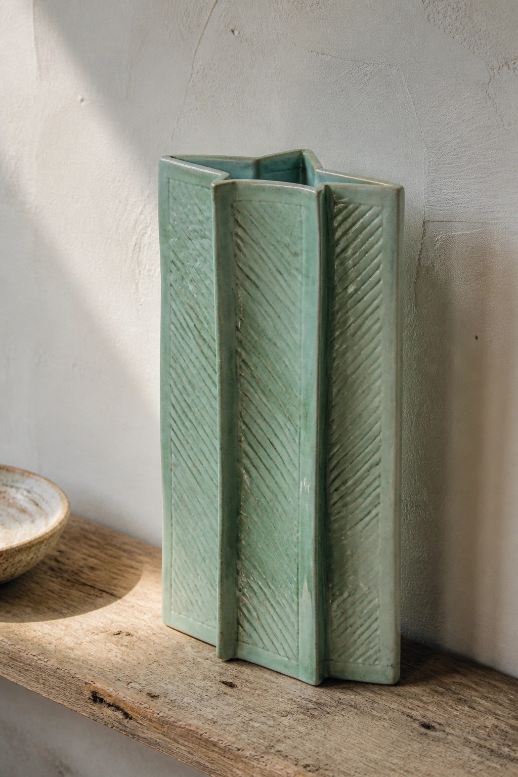 Mint green faceted ceramic vase with herringbone patterns on wooden shelf