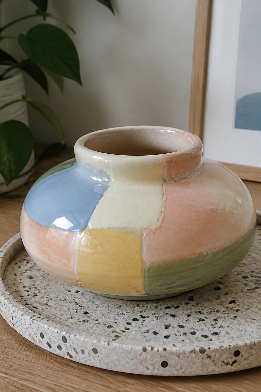 Pastel patchwork ceramic vase on speckled terrazzo tray with wooden backdrop