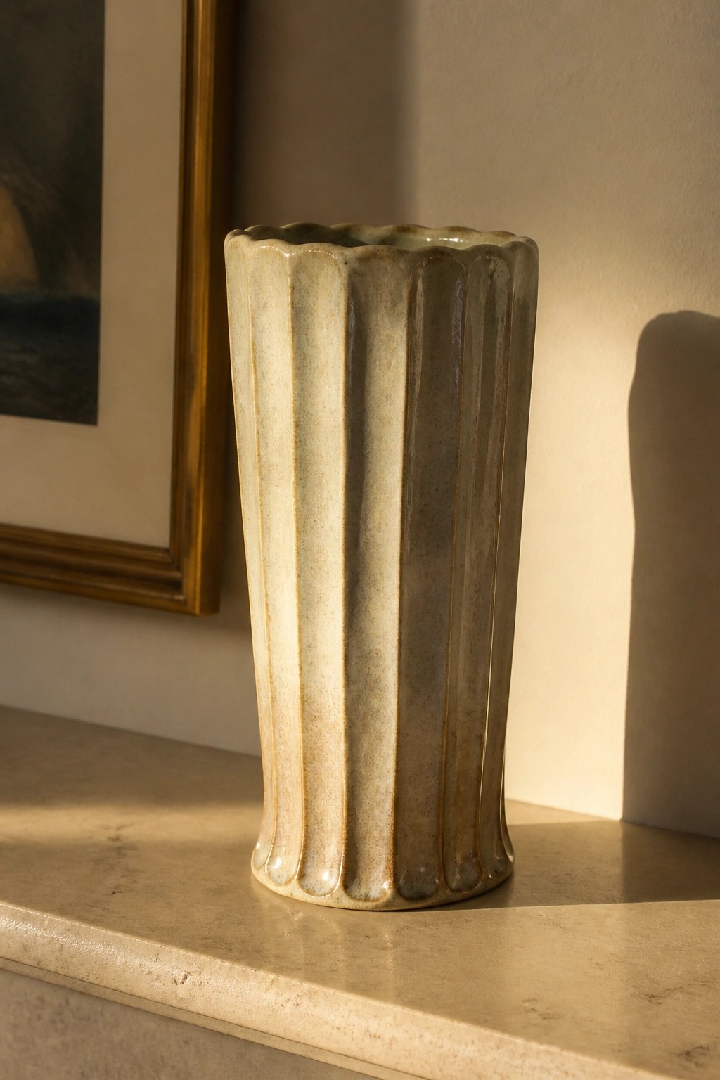 Fluted beige ceramic vase on sunlit marble ledge with shadows