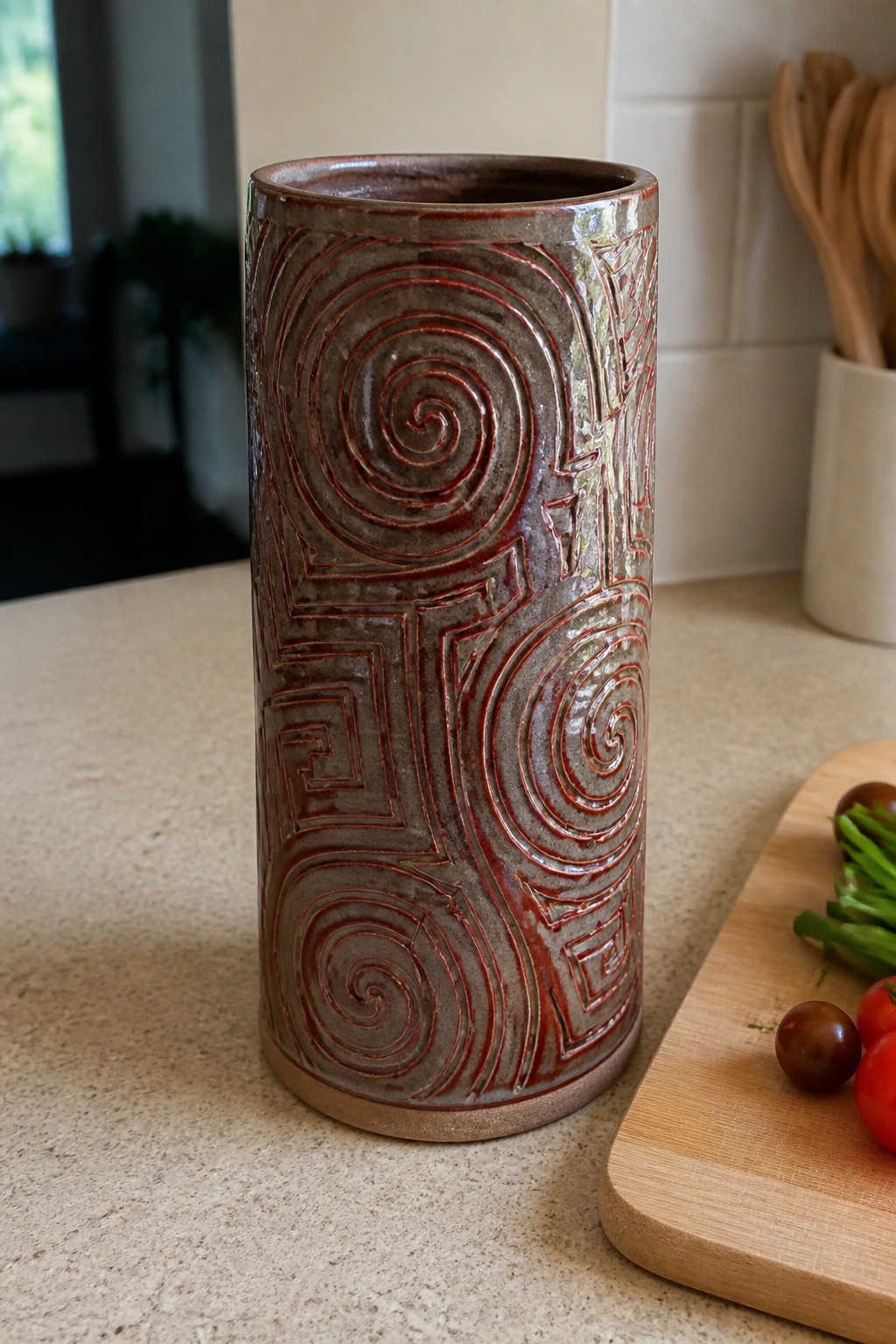 Tall ceramic vase with red spiral patterns on kitchen counter near cutting board