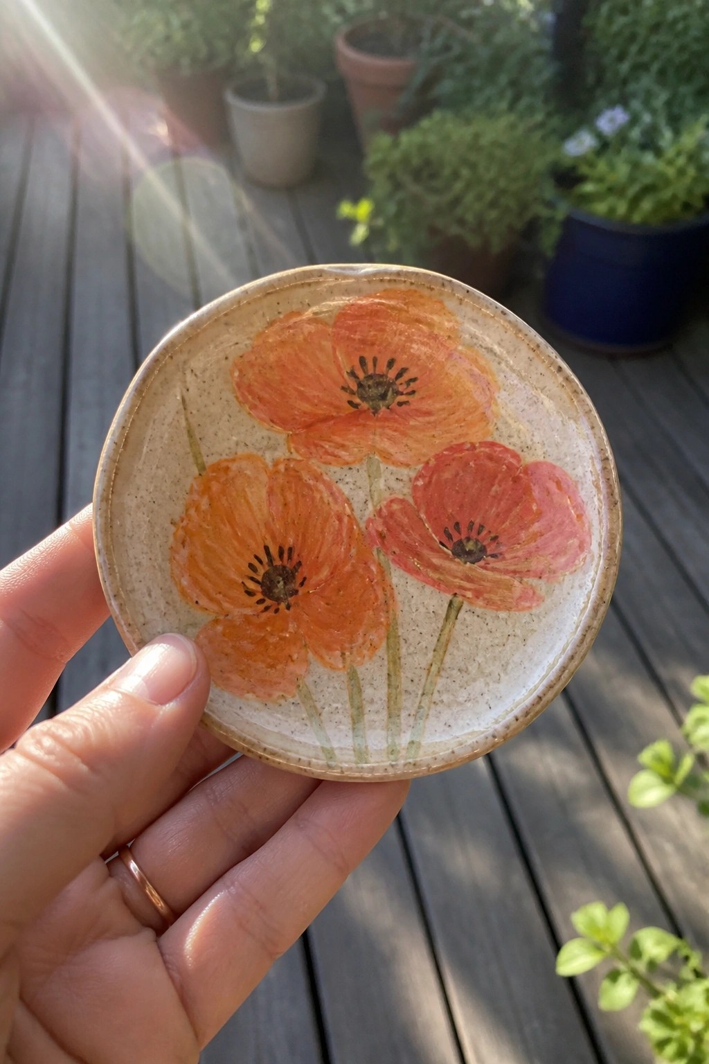 Hand holding speckled ceramic plate painted with orange poppies on sunny deck