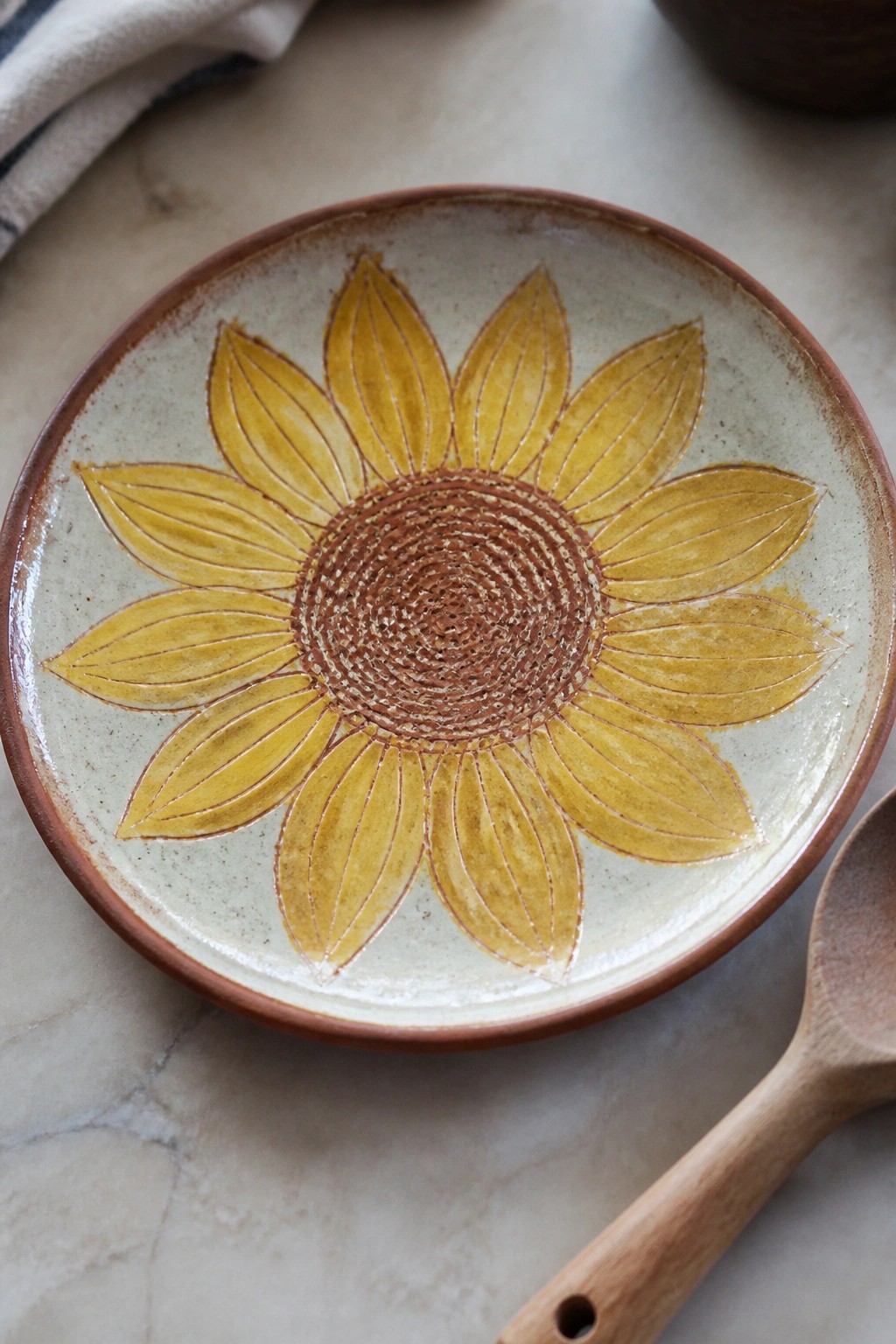 Ceramic bowl with yellow sunflower design beside wooden spoon on marble surface.