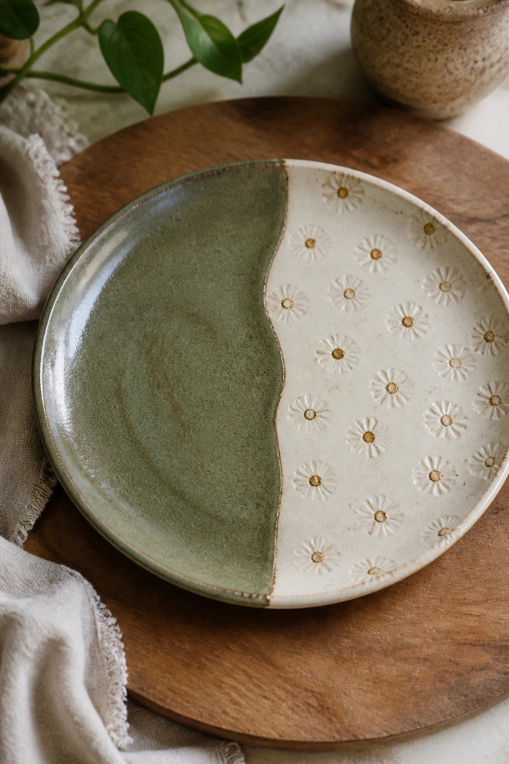 Sage green and cream ceramic plate with daisy imprints on wooden board
