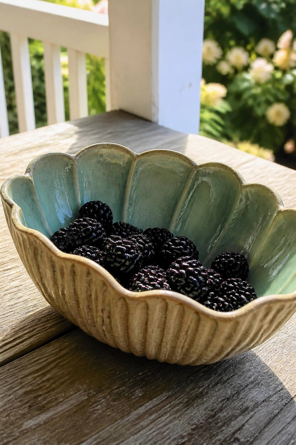 Scalloped ceramic bowl filled with ripe blackberries on sunlit wooden table.