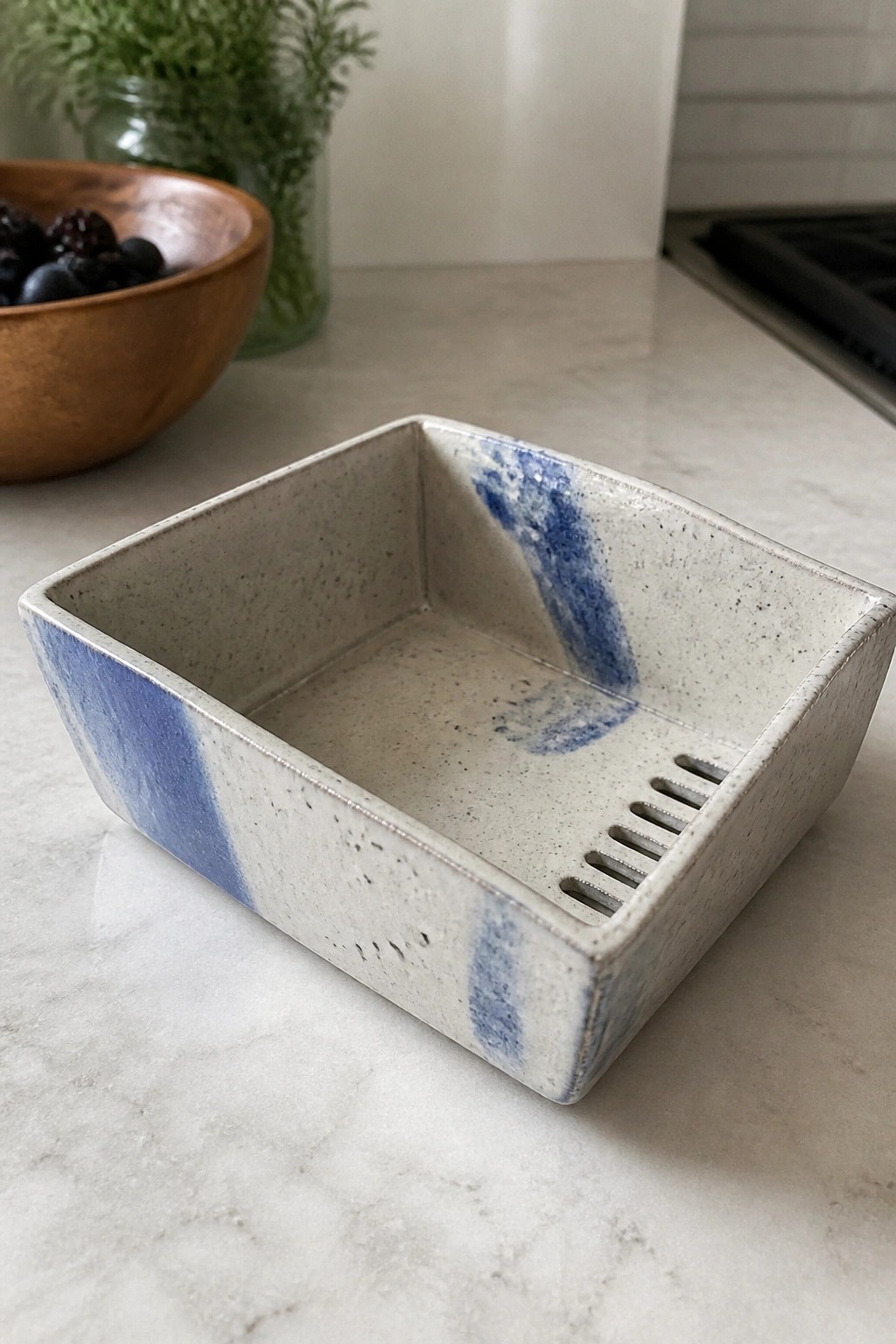 Square speckled ceramic dish with blue glaze and side slits on marble counter.