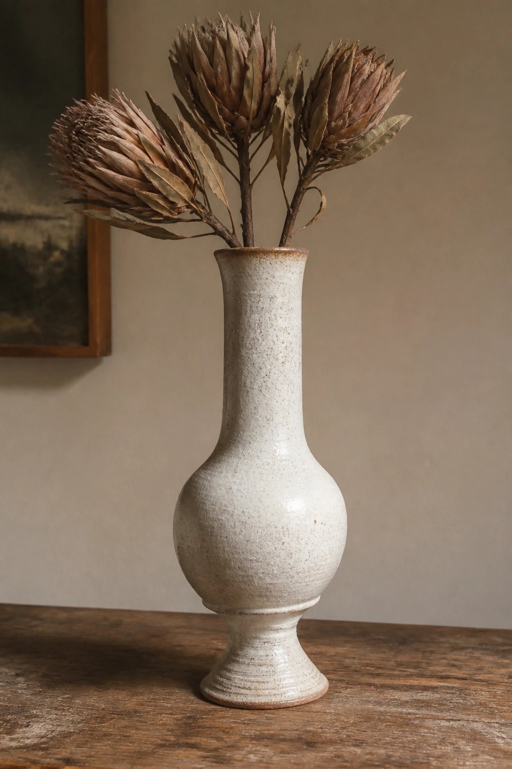 Speckled white ceramic vase with dried brown flowers on wooden table