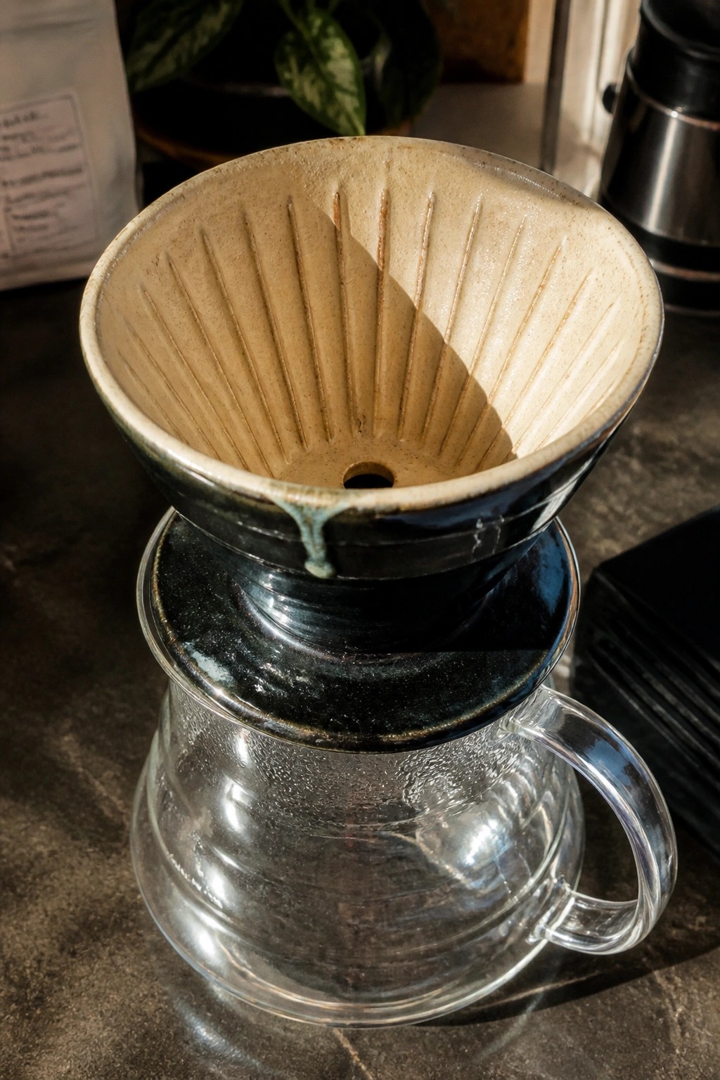 Ceramic coffee dripper with ridged beige interior atop glass carafe in sunlight