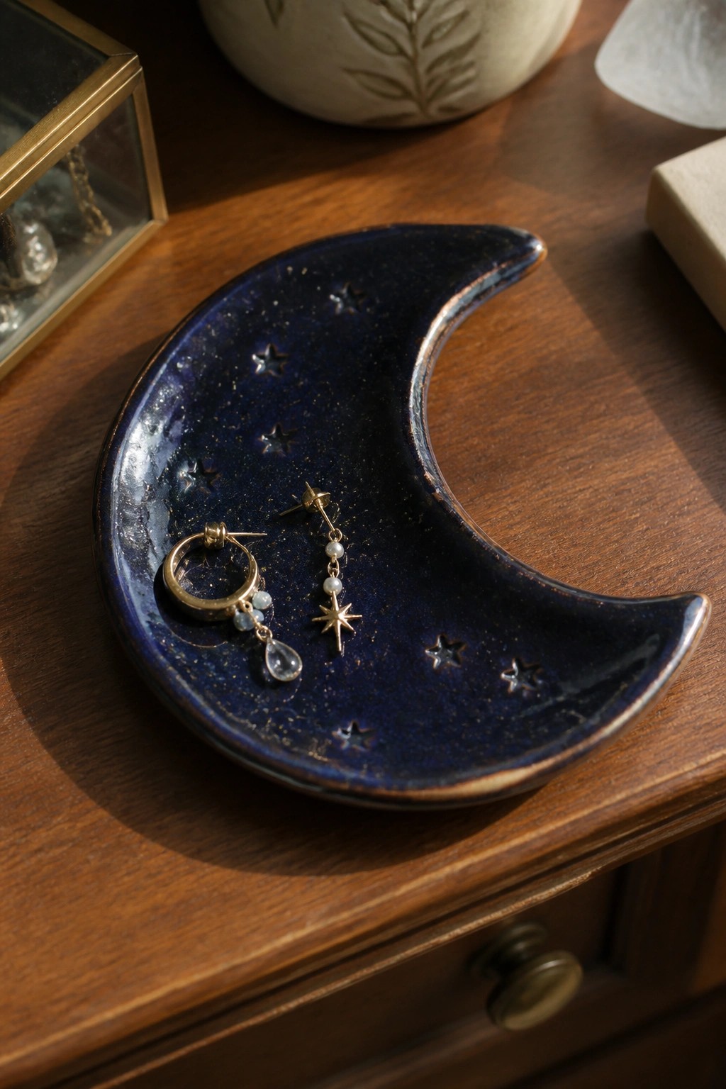 Blue crescent moon dish with star motifs holding gold earrings on wood.