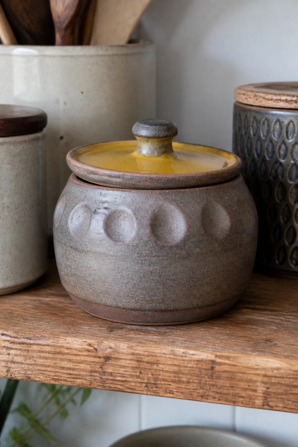 Gray ceramic jar with yellow lid and dotted pattern on wooden shelf