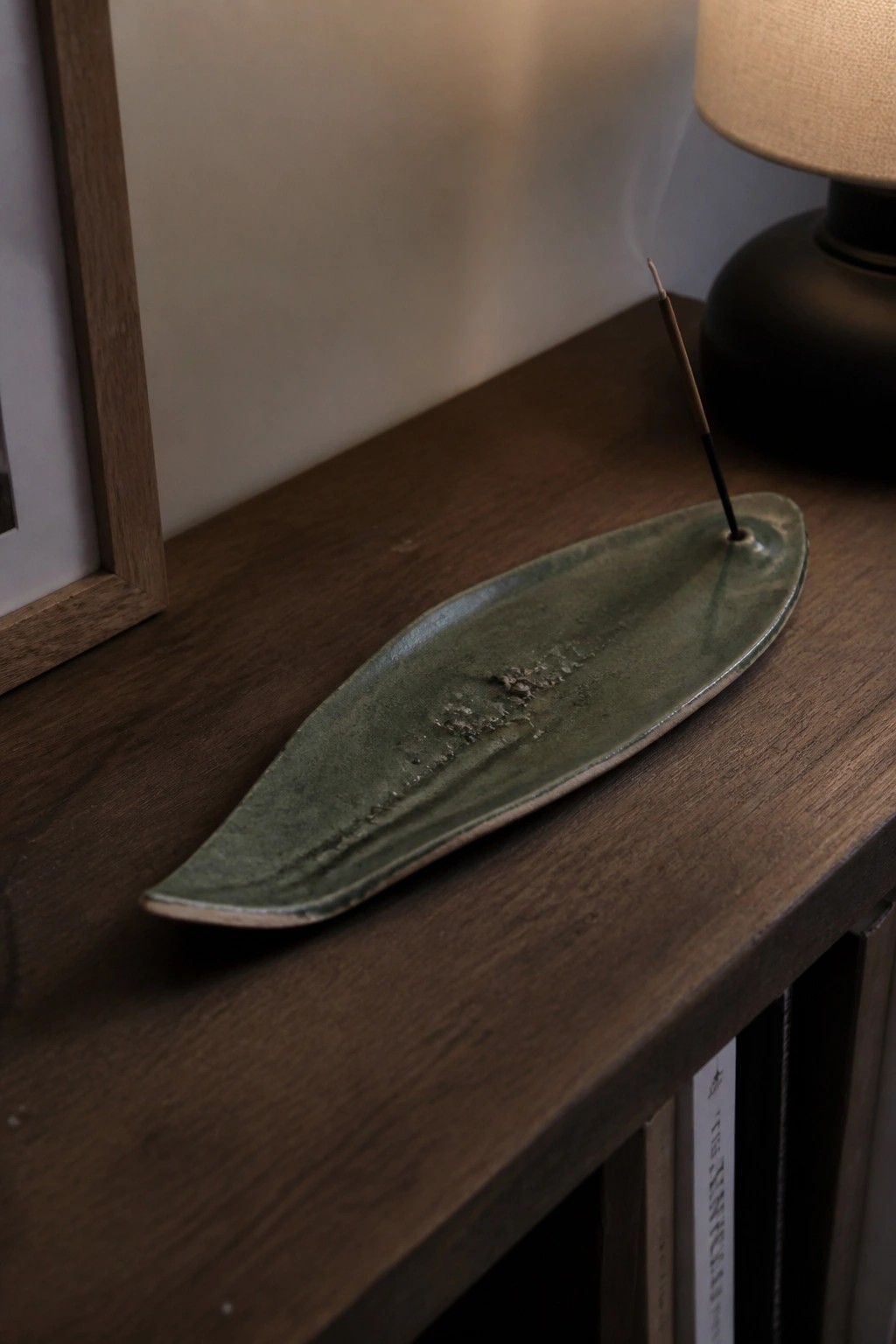 Green ceramic leaf-shaped incense holder with burning stick on wooden table