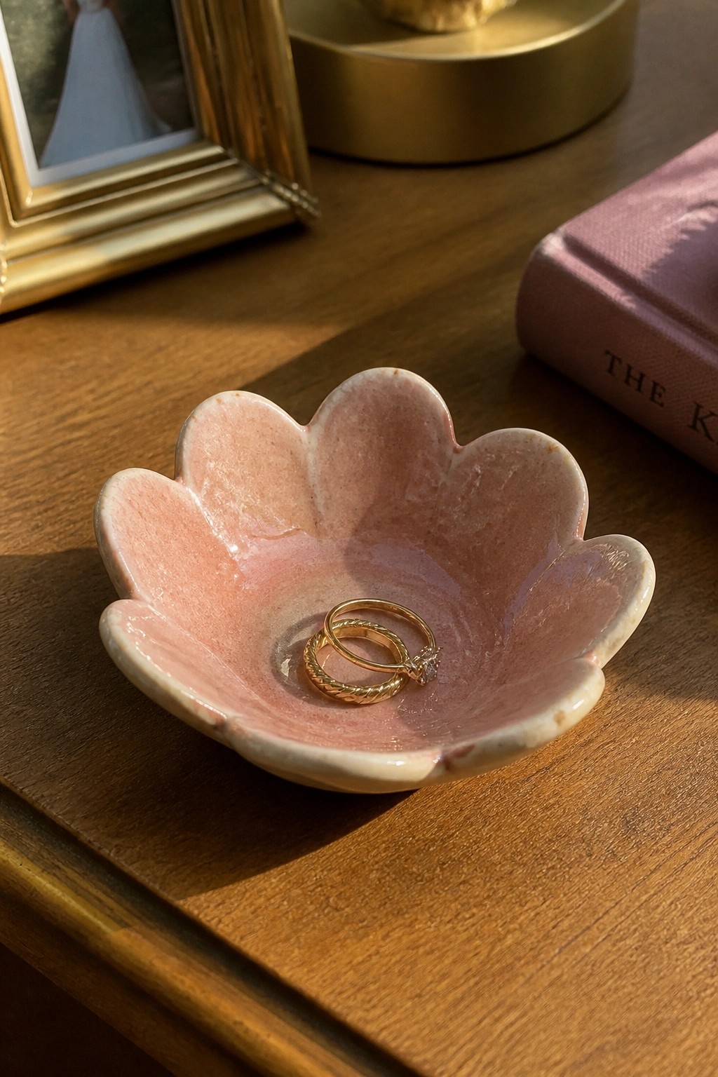 Pink flower-shaped ceramic bowl holding two gold rings on wooden table