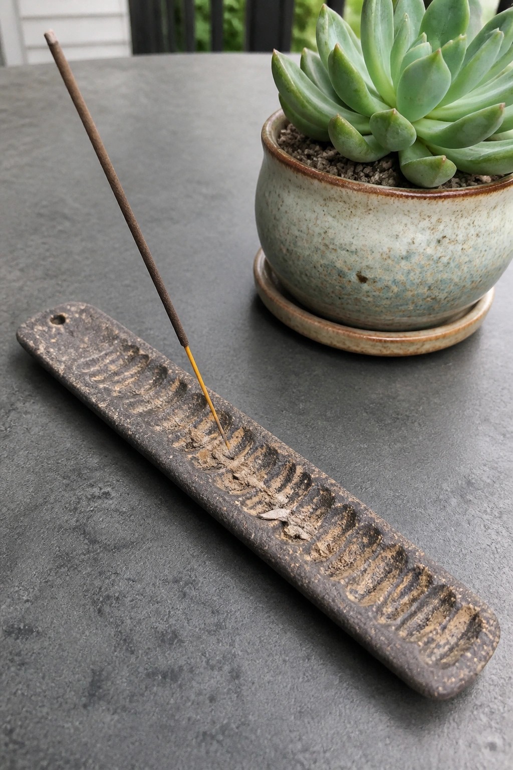 Burning incense stick in a rustic holder beside a potted green succulent