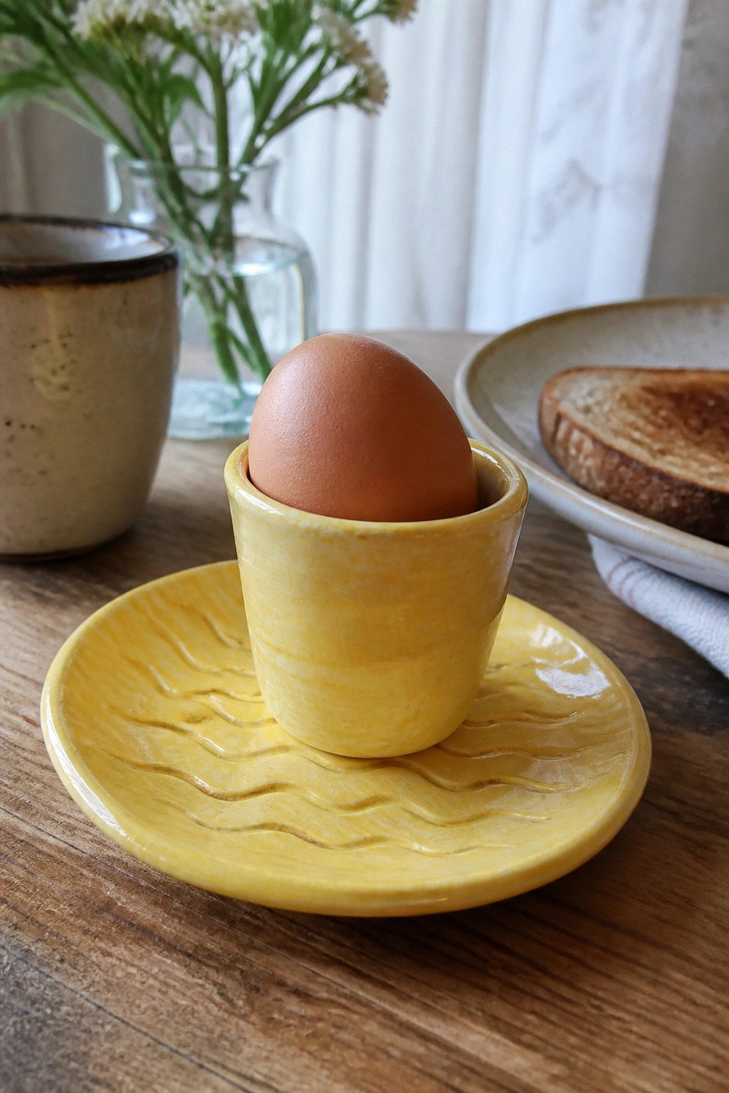 Brown egg in bright yellow ceramic cup on wavy saucer atop wooden table