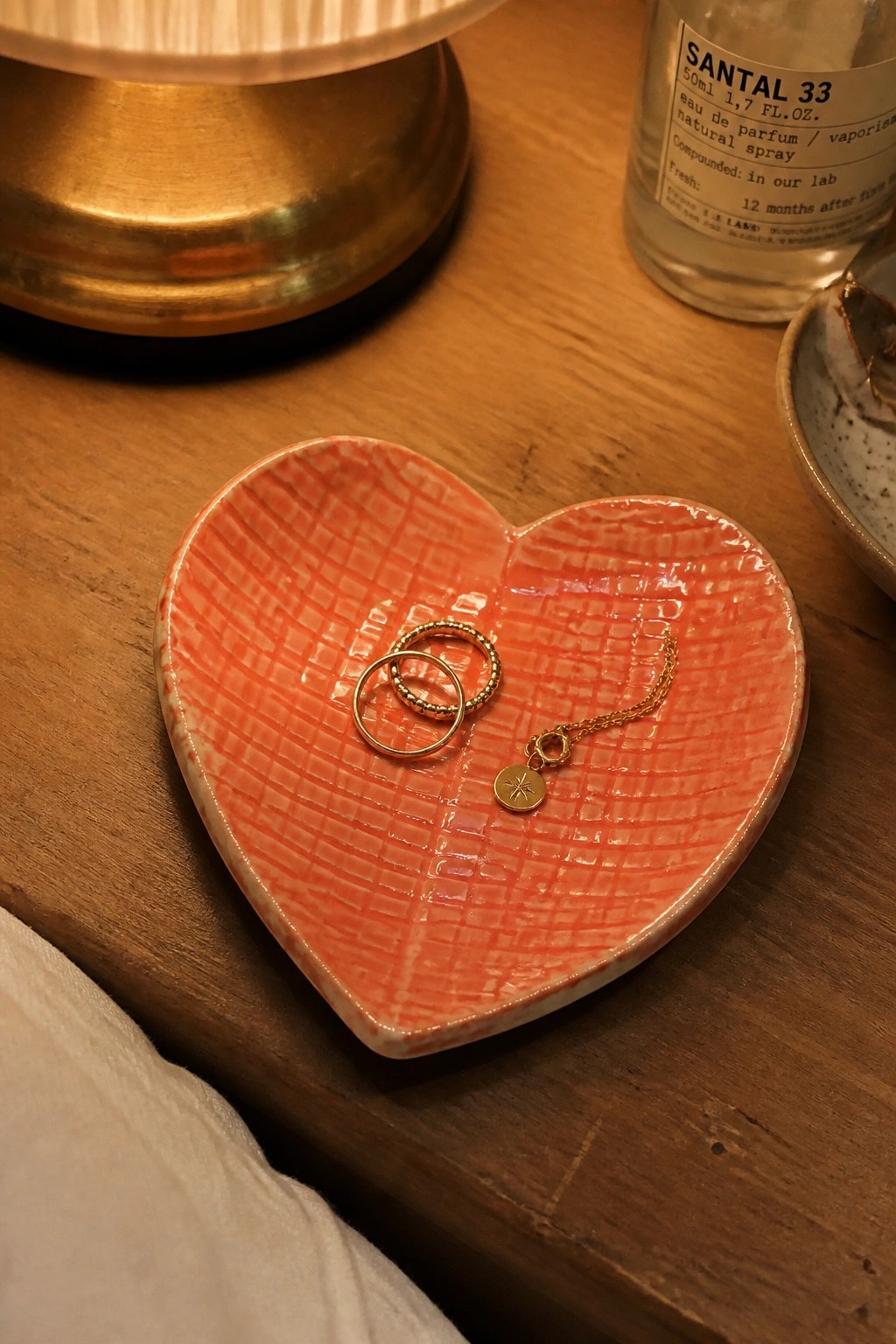 Heart-shaped coral ceramic dish holding gold rings and star necklace on wood