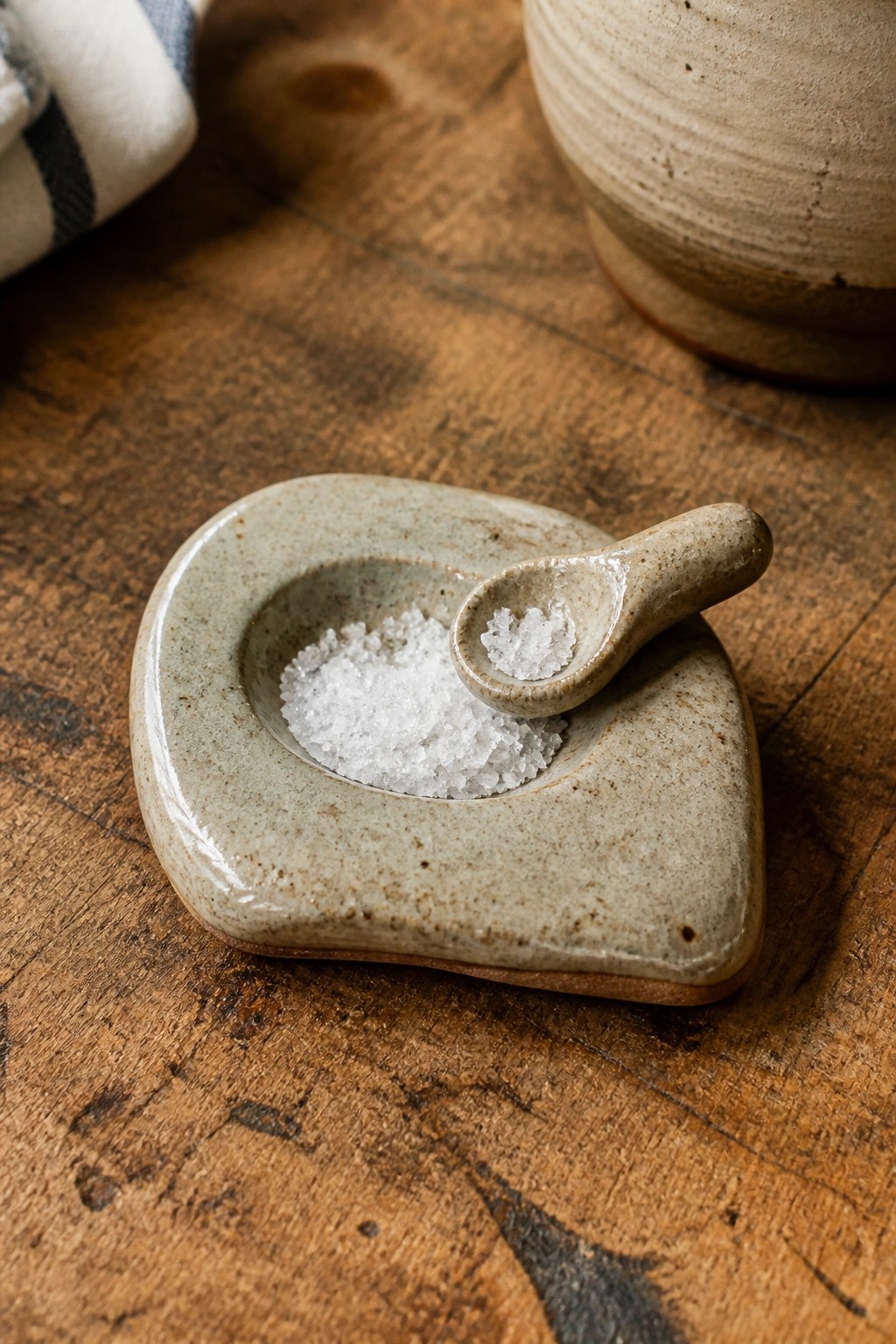 Ceramic salt cellar with spoon of white crystals on rustic wooden table
