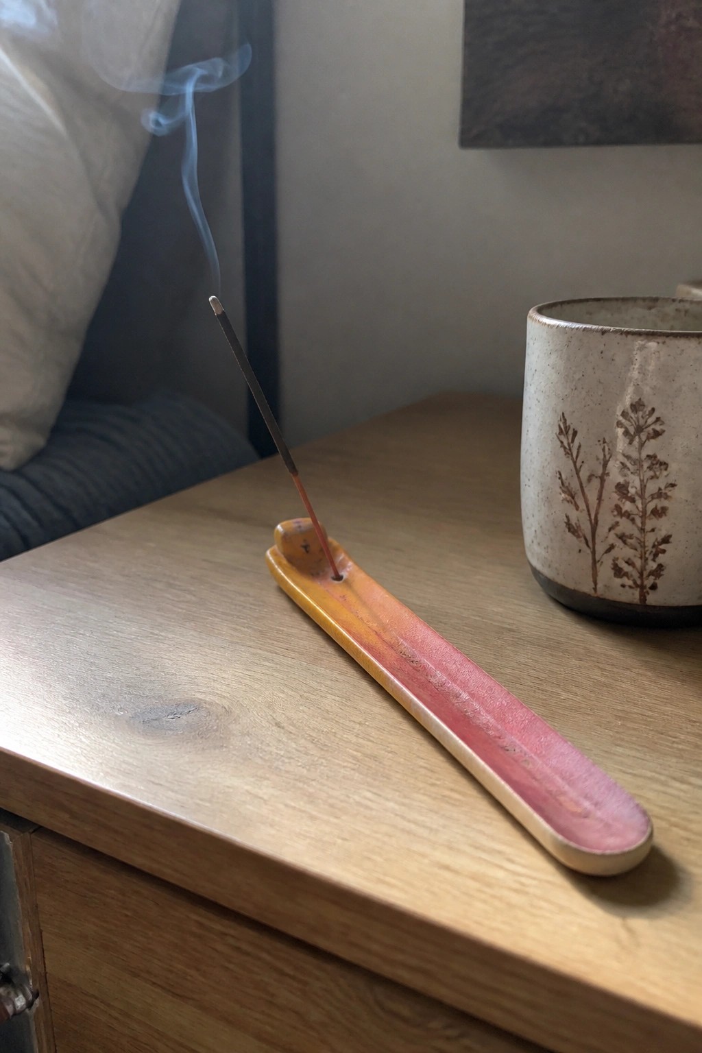 Burning incense stick in colorful ceramic holder beside patterned mug on wood table