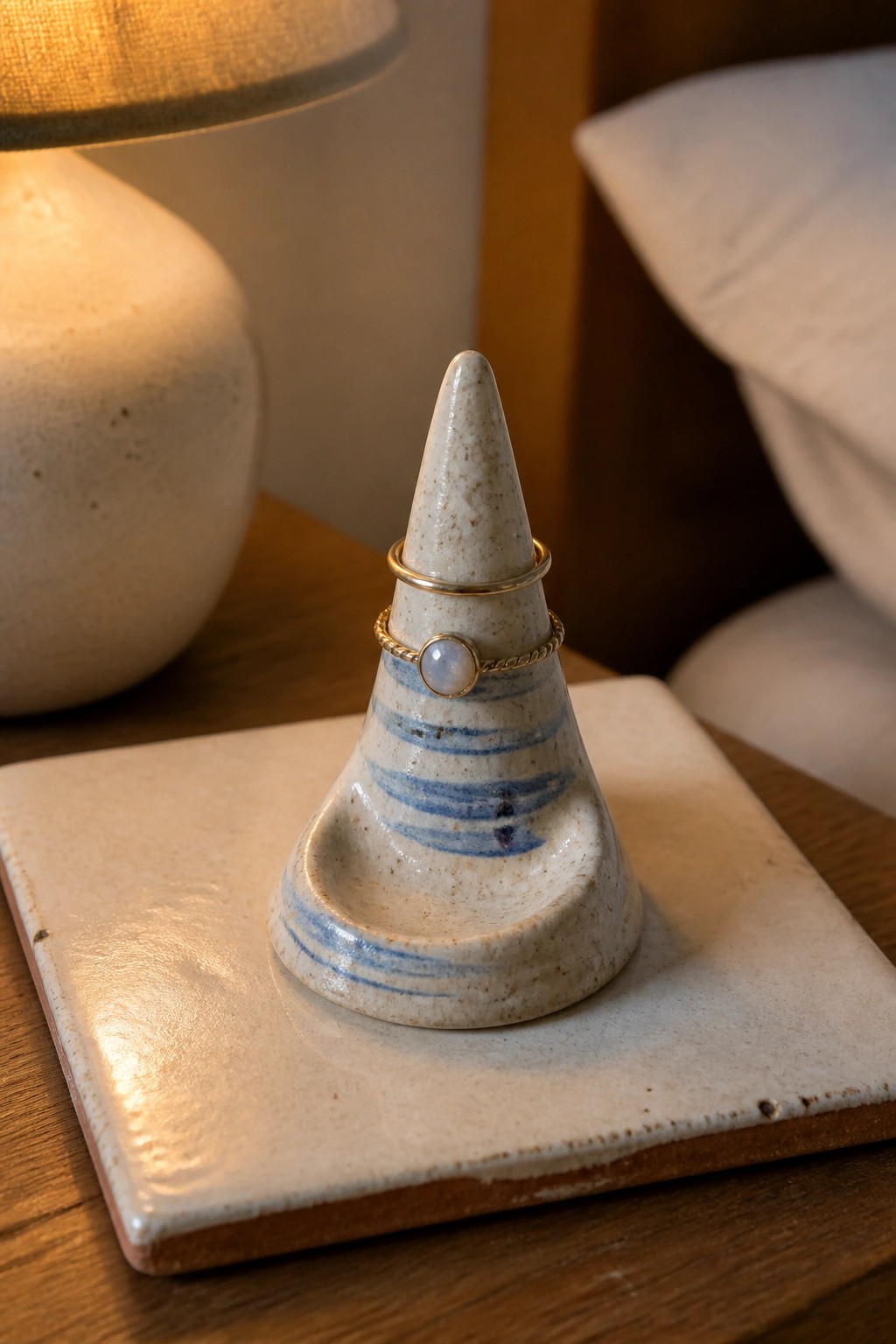 Ceramic cone ring holder with two gold rings on wooden nightstand