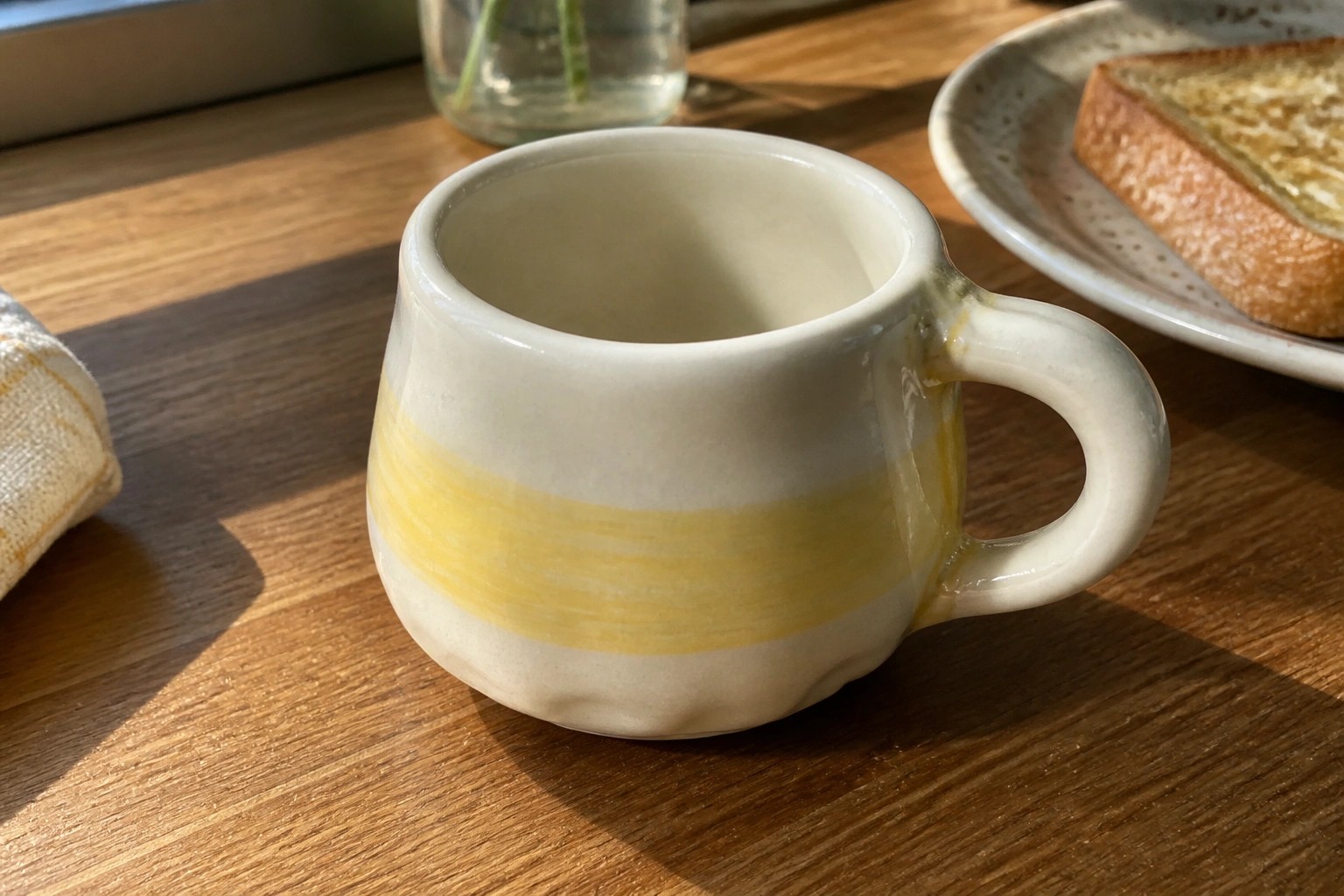 Small white ceramic mug with yellow stripe on sunlit wooden table